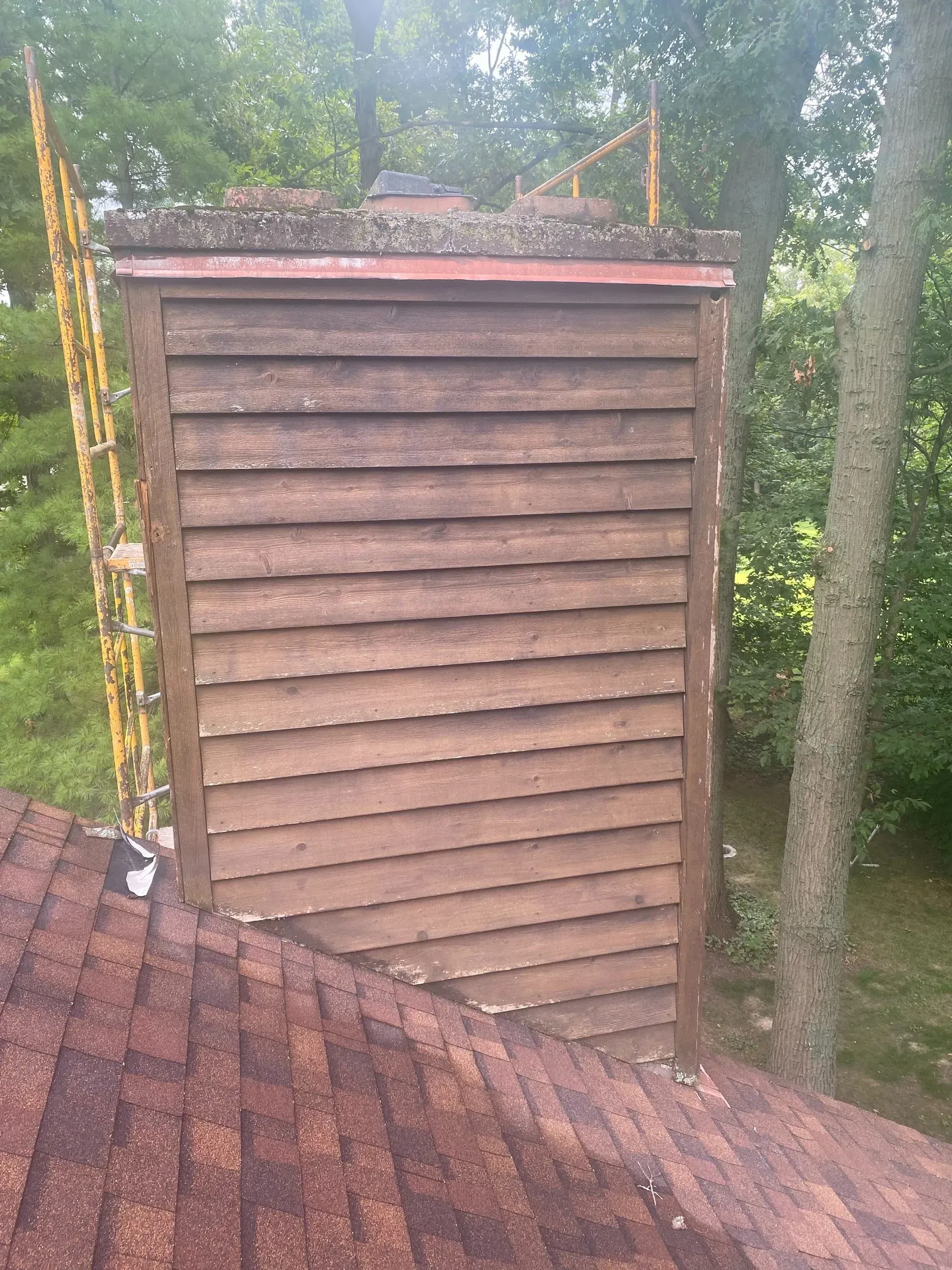 A wooden shed is sitting on top of a roof next to trees.