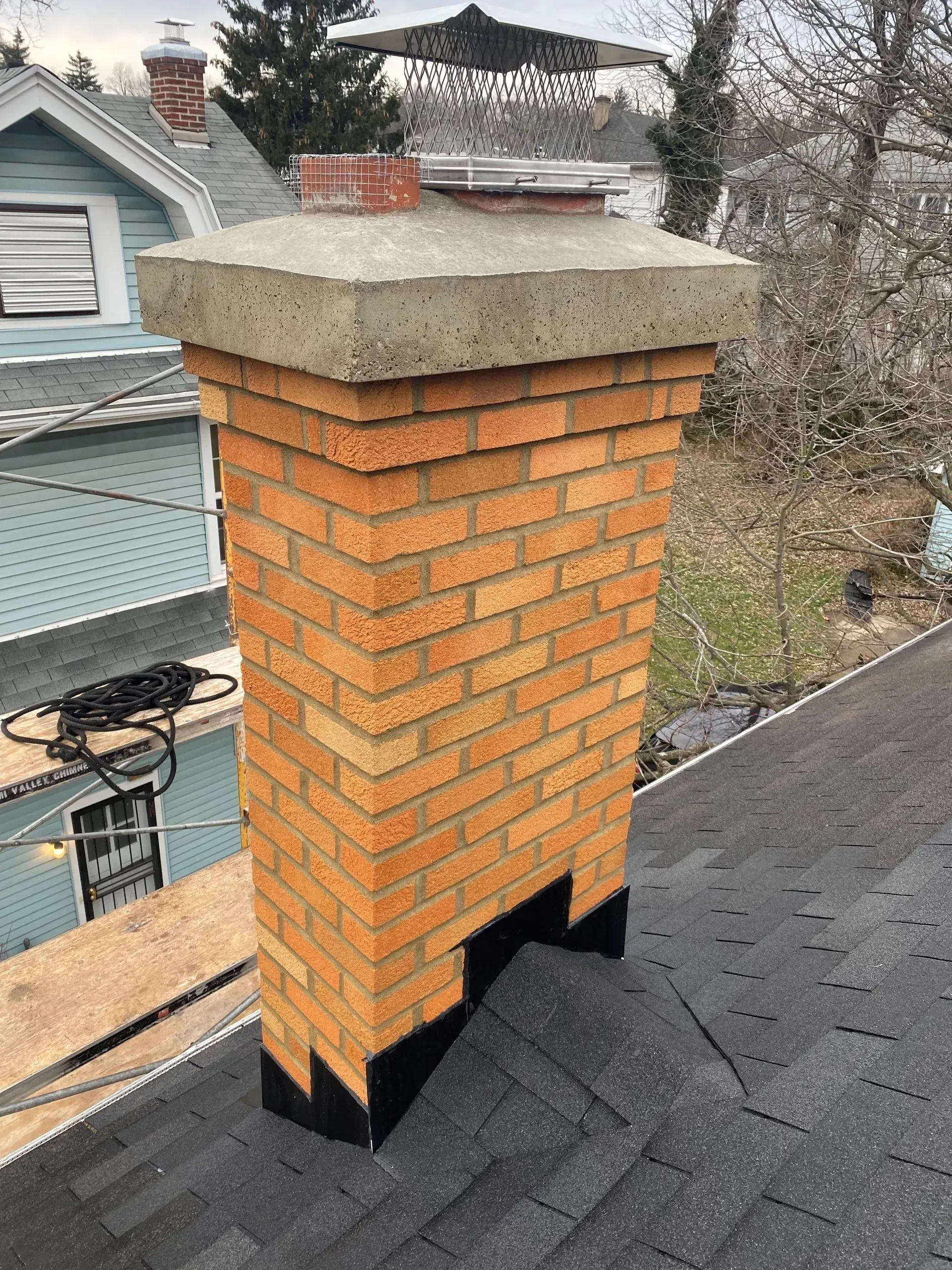 A brick chimney is sitting on top of a roof next to a house.