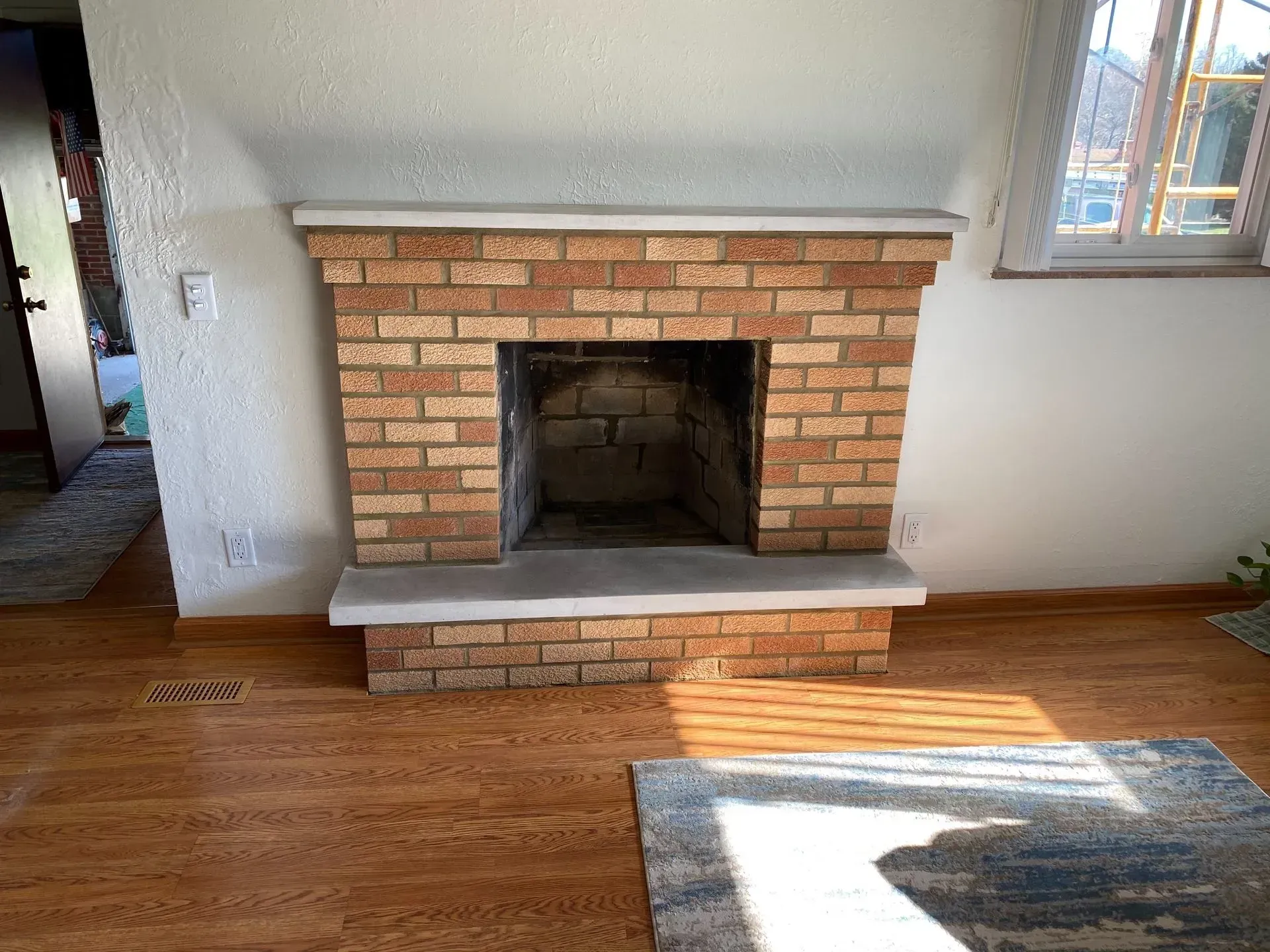 A living room with a brick fireplace and a rug.