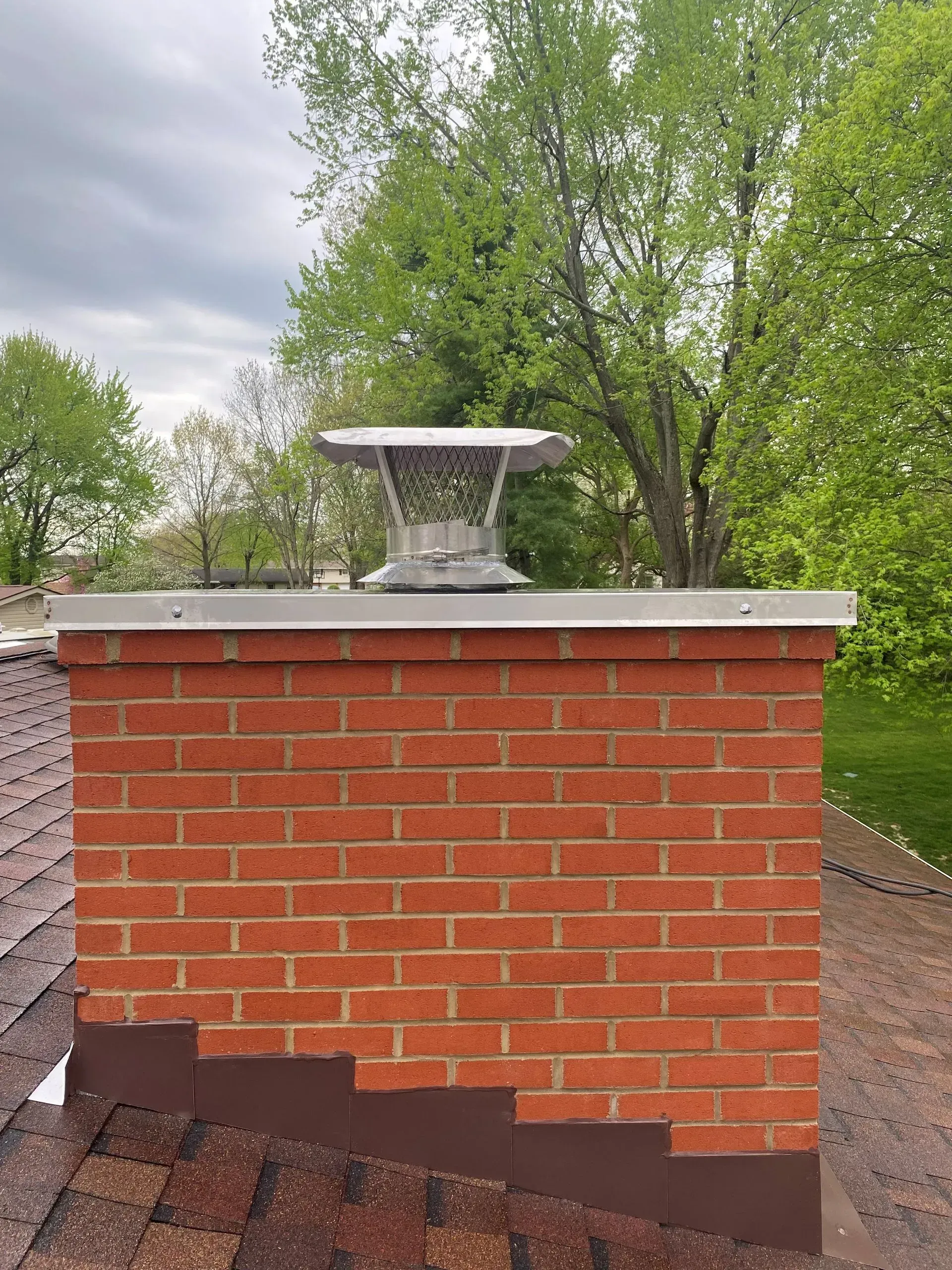 A brick chimney on top of a roof with trees in the background