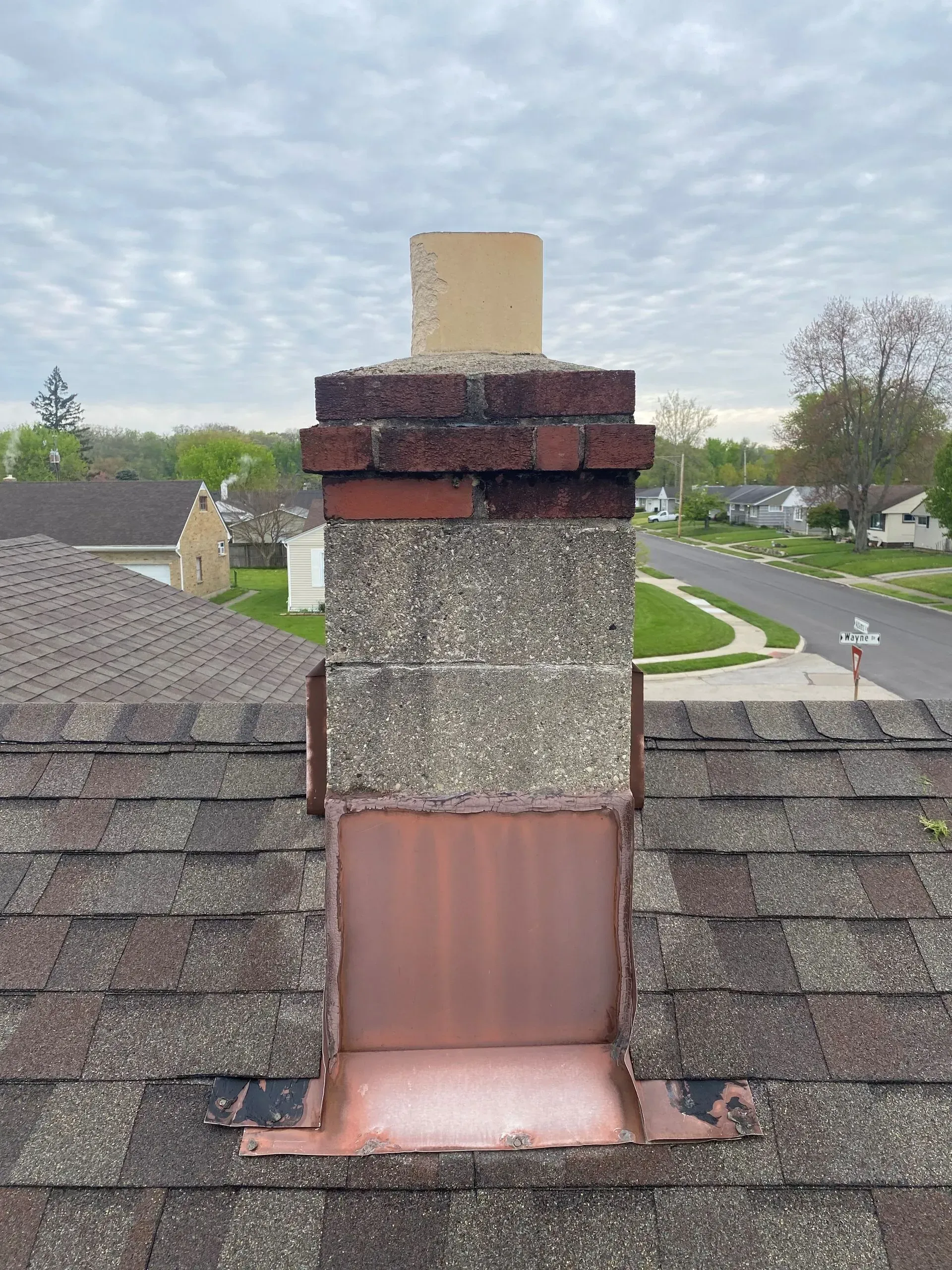 A chimney on top of a roof with a copper cover on it.