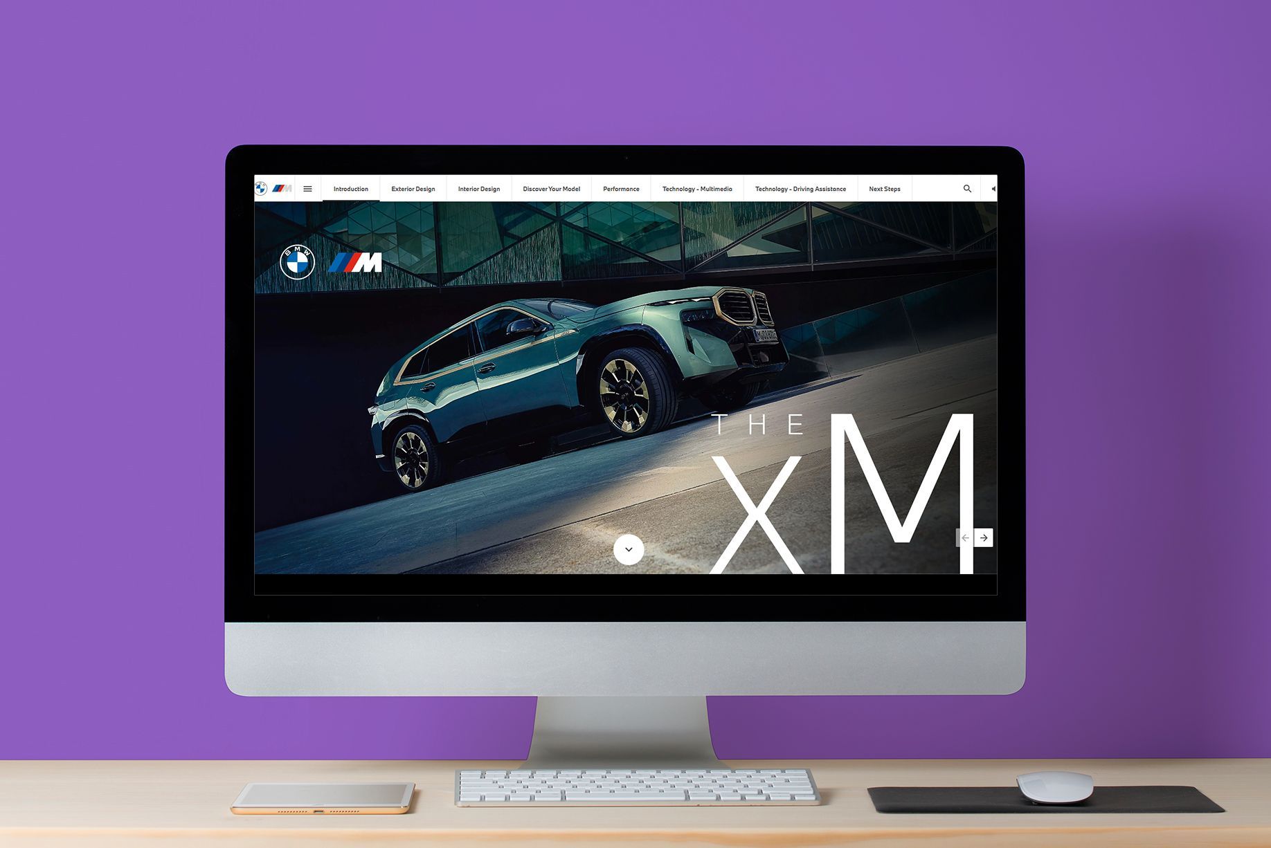 BMW XM on a computer screen, displayed on a desk against a purple wall.