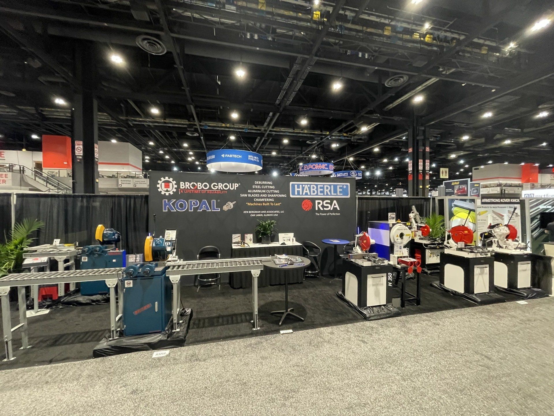 A trade show booth with machinery on display, featuring a black backdrop with logos and product demonstrations.