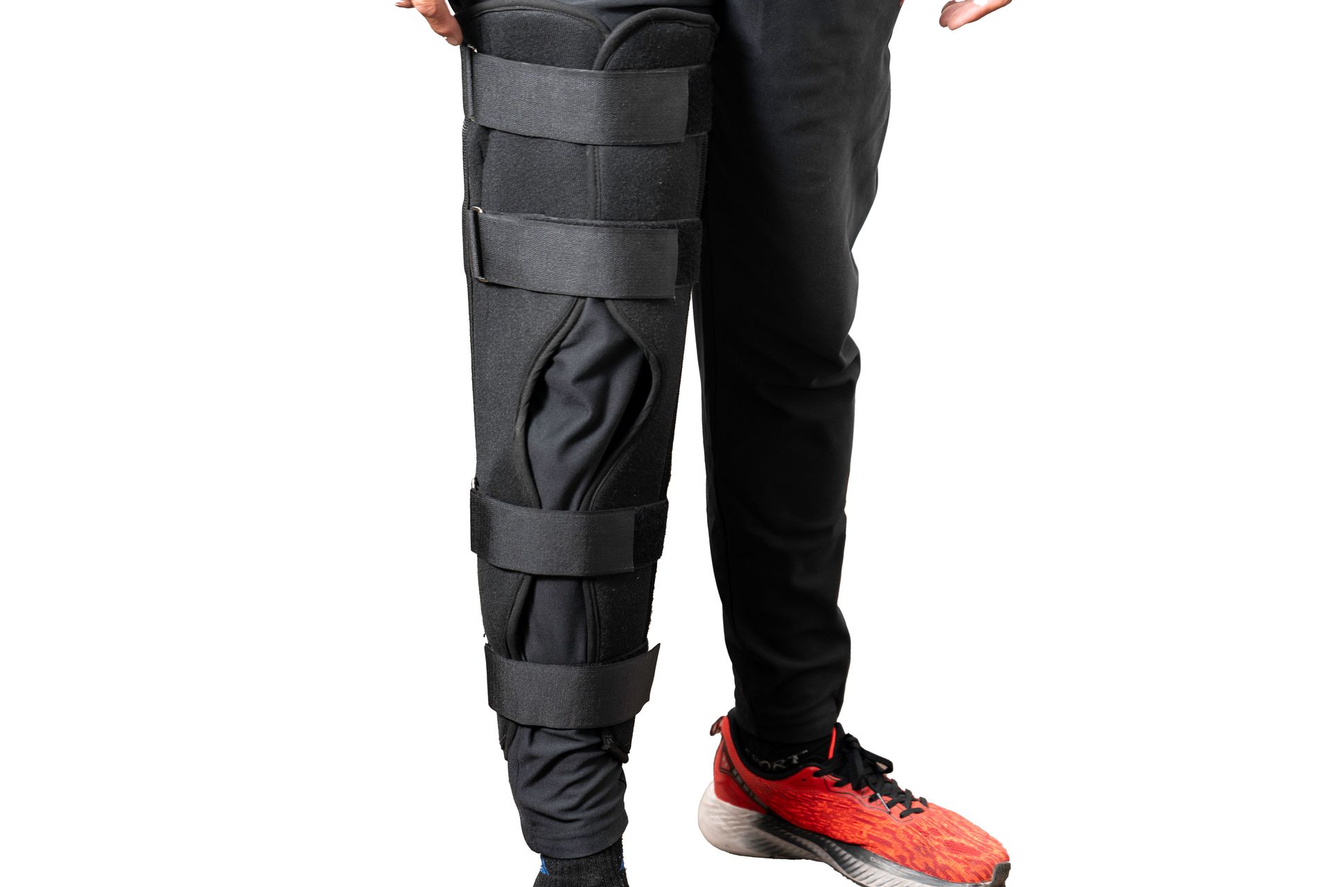 Persona que lleva un aparato ortopédico de color negro en la pierna sobre un pantalón negro y un zapato rojo.