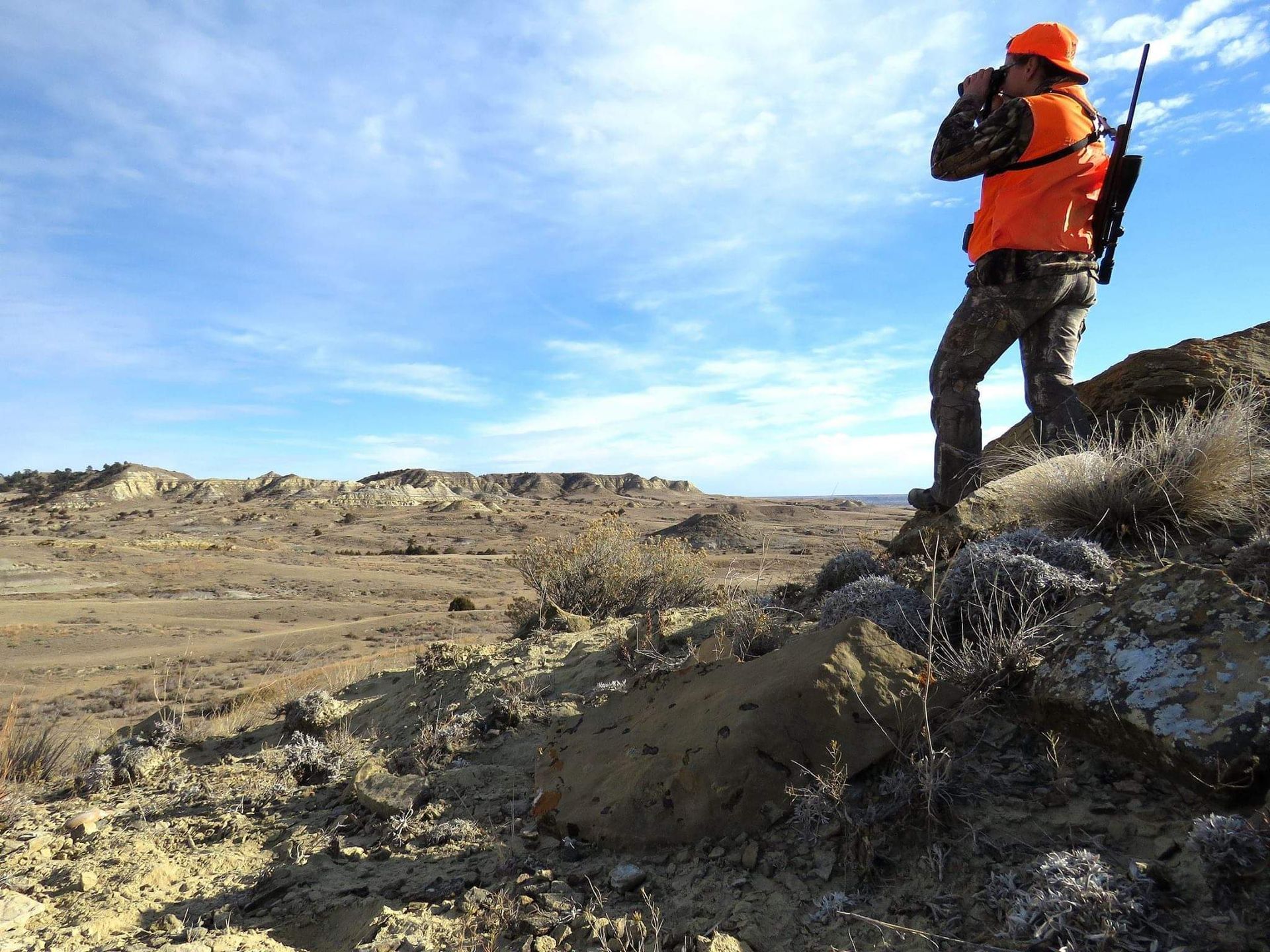 a man in an orange vest is standing on a rock in the desert