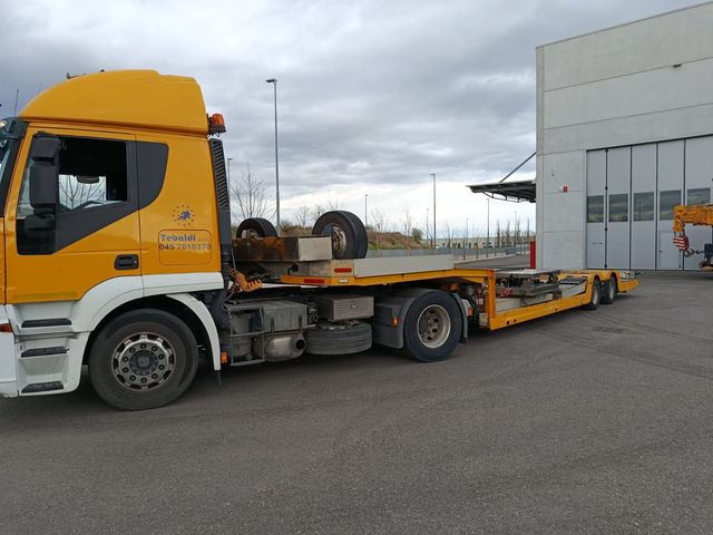 Autocarro gru Iveco giallo parcheggiato all'aperto sul marciapiede.