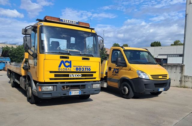 Autocarro gru Iveco giallo parcheggiato all'aperto sul marciapiede.
