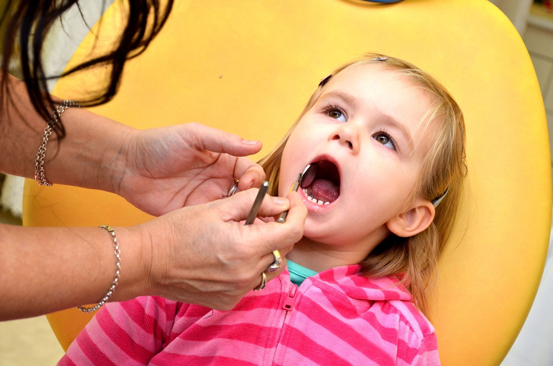 Un dentista visita un bambino sorridente in una clinica, con una mano guantata di blu e strumenti odontoiatrici.