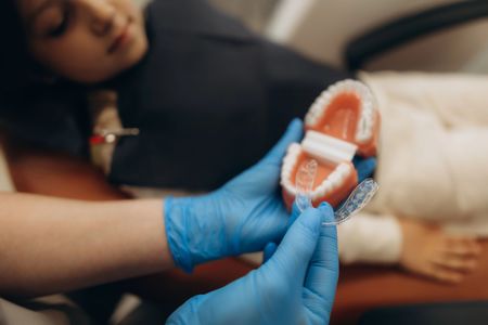 Mani guantate che reggono un calco dentale accanto a un paziente sdraiato in un ambiente clinico.