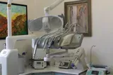 Sala visite odontoiatriche con poltrona reclinabile e attrezzature mediche accanto a una cartella clinica a parete.