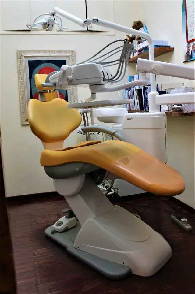 Poltrona odontoiatrica con rivestimento arancione in una clinica, mostrata con lampade per esame e strumenti collegati.