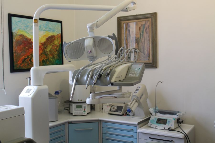 Studio dentistico con poltrona odontoiatrica, lampada a soffitto e armadietti sotto quadri appesi alla parete.