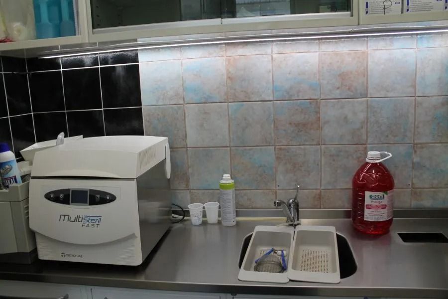 Bancone della cucina con lavello, dispenser di sapone e un elettrodomestico bianco accanto a una bottiglia di bevanda rossa.