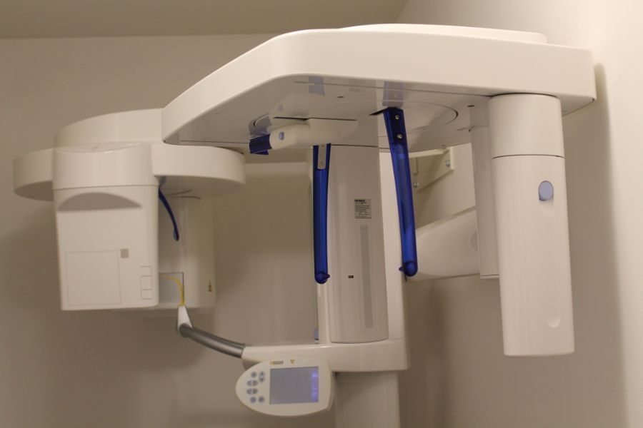 Apparecchio radiografico dentale con maniglie blu montato a parete in una stanza della clinica.
