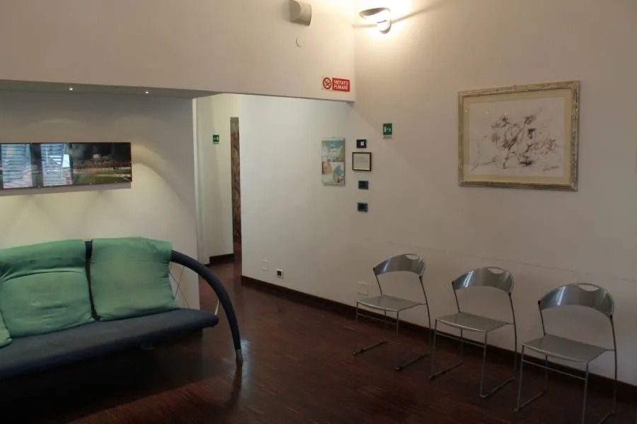 Piccola sala d'attesa con divano color verde acqua, tre sedie in metallo, quadri alle pareti e pavimento in legno scuro.