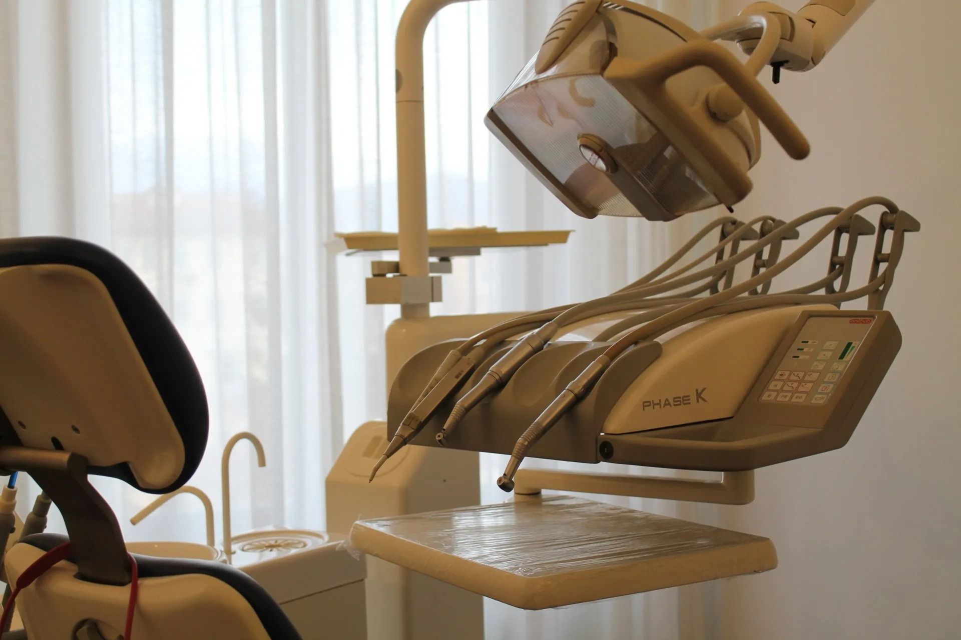 Poltrona odontoiatrica e lampada da visita a soffitto in una clinica, con una finestra sullo sfondo.