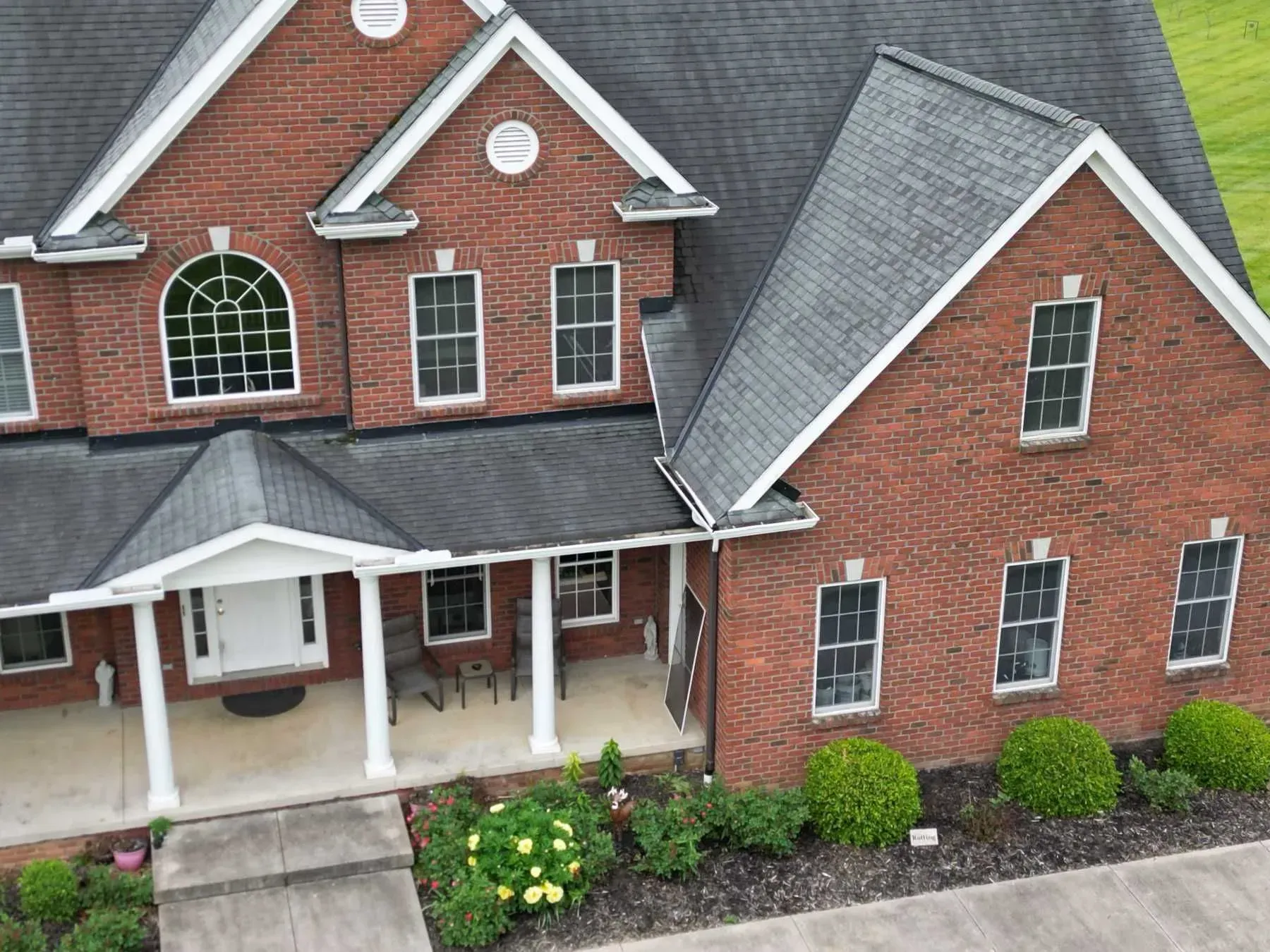Brick house with dark roof and white trim. Front porch with columns and garden in front.