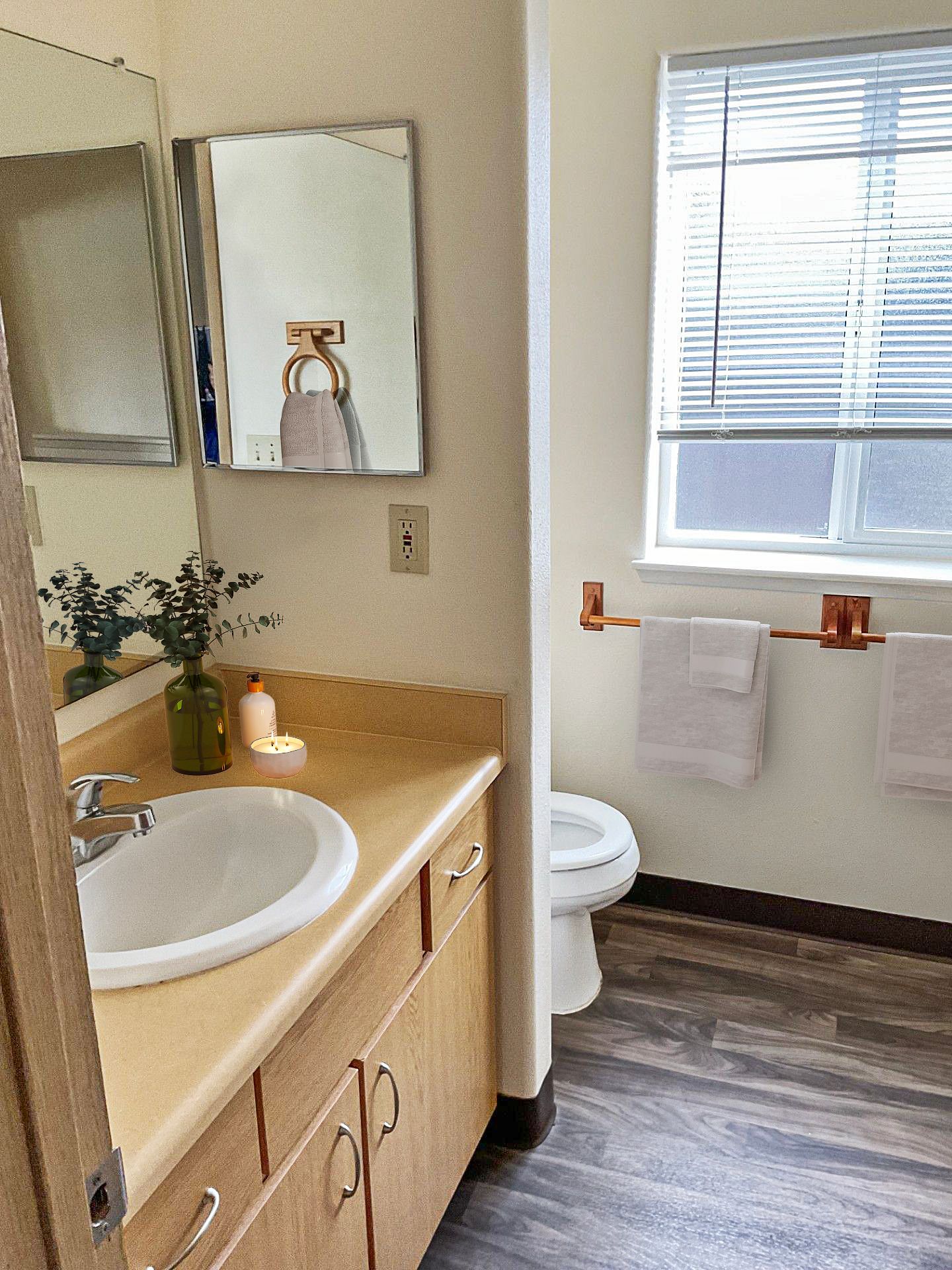 A bathroom with a sink , toilet , mirror and window.