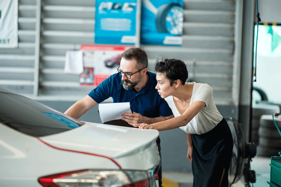 A Man and A Woman Are Looking at A Car in A Garage.