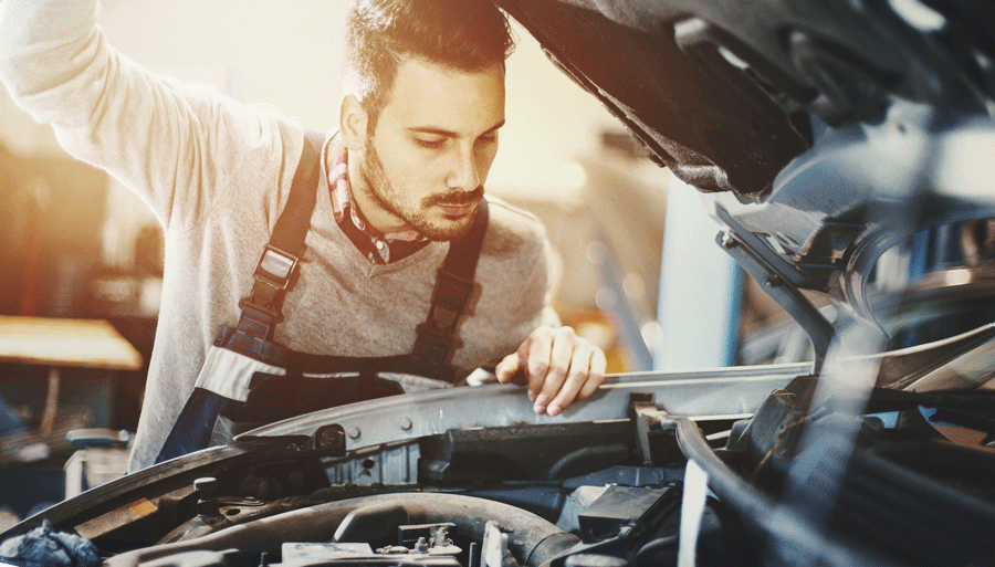 A Man Is Working on A Car in A Garage with The Hood Open.