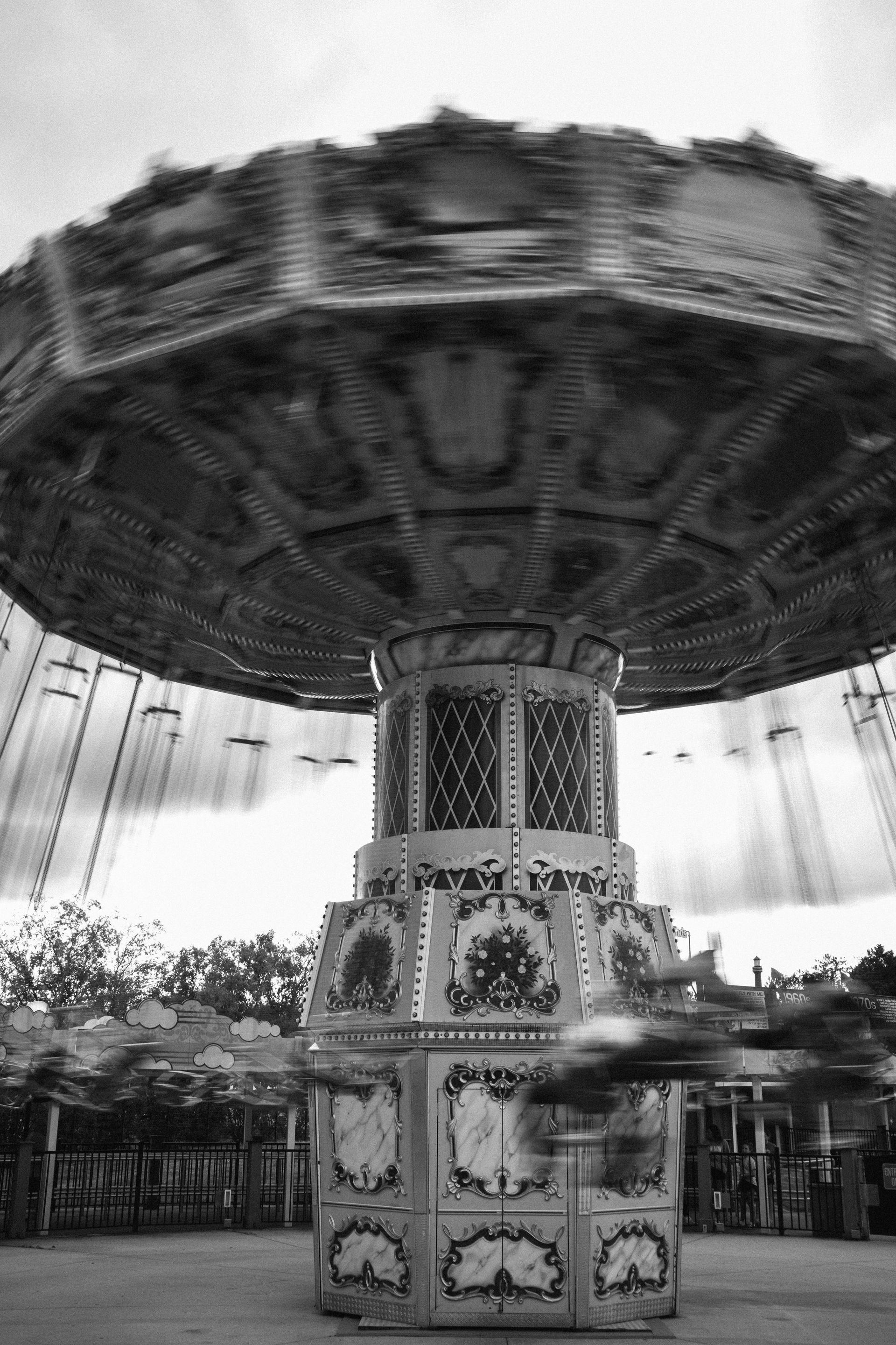 A black and white photo of a spinning carousel ride at an amusement park.