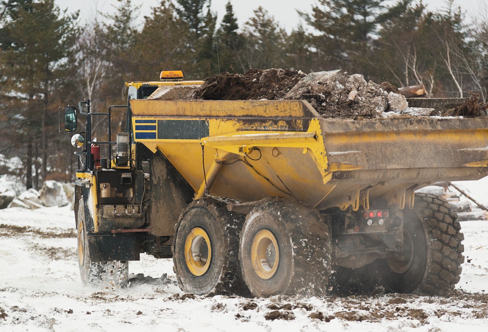 A yellow dump truck is driving through a snowy field