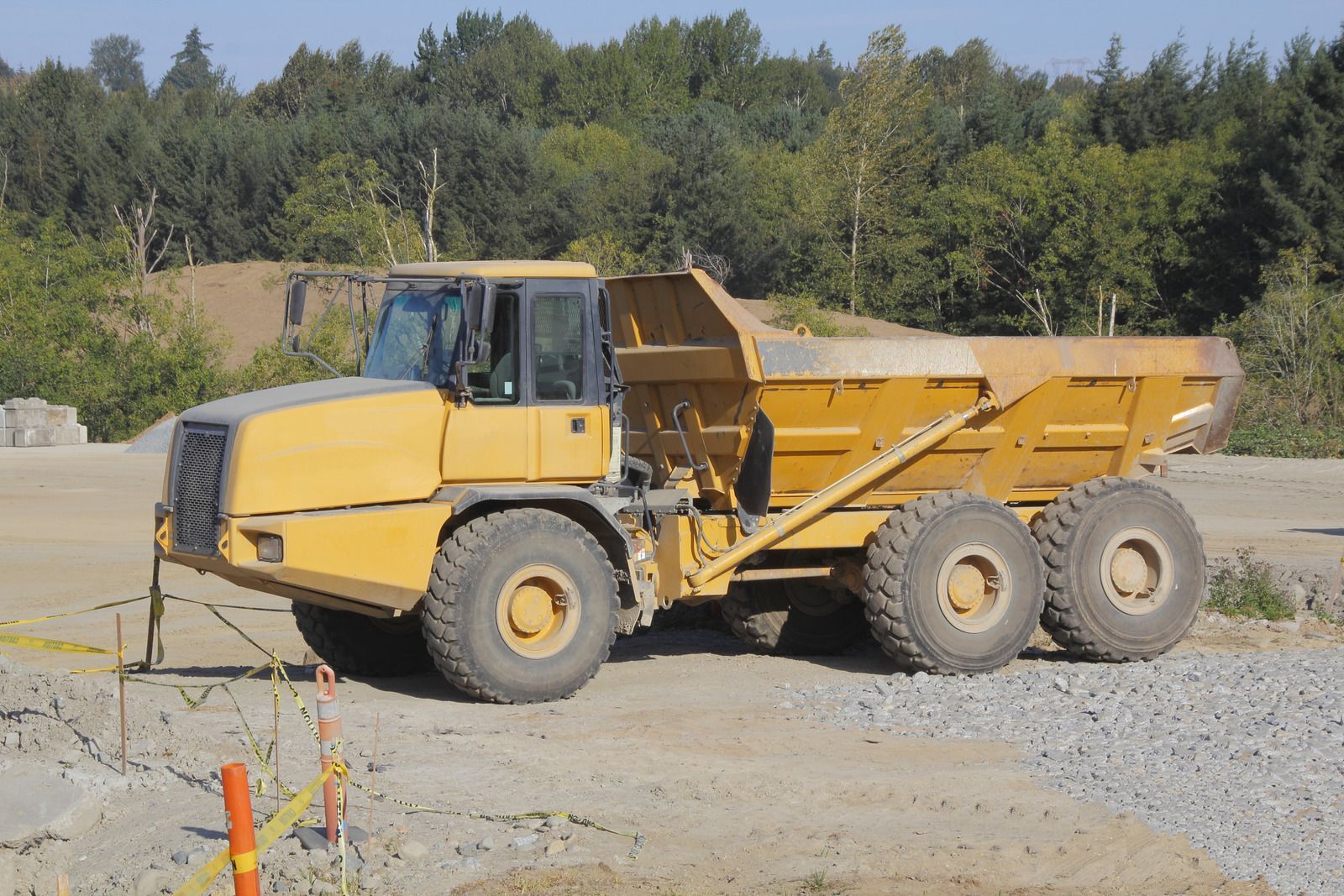 A yellow dump truck is parked in a dirt field