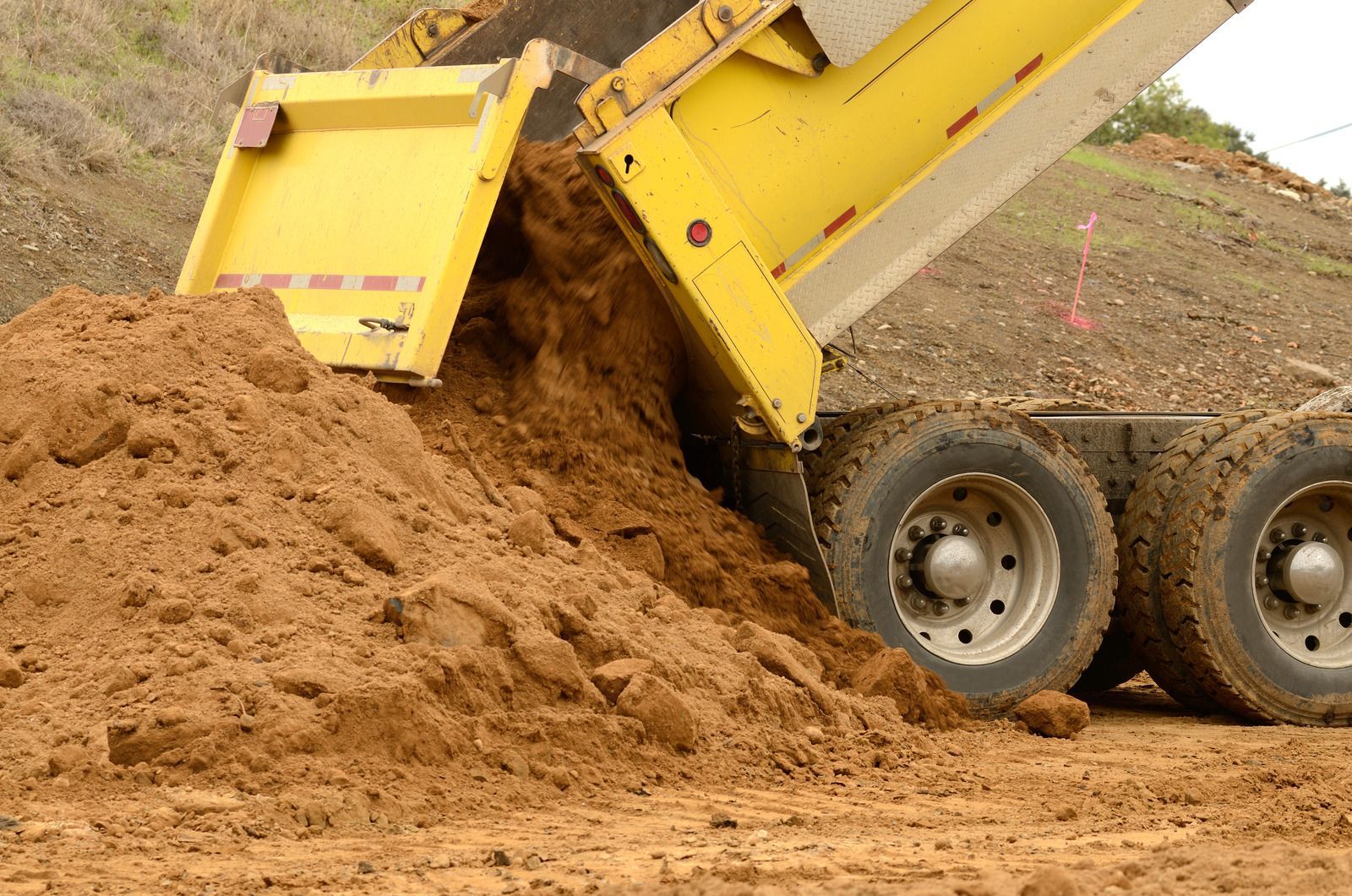 A yellow dump truck is dumping dirt into a pile
