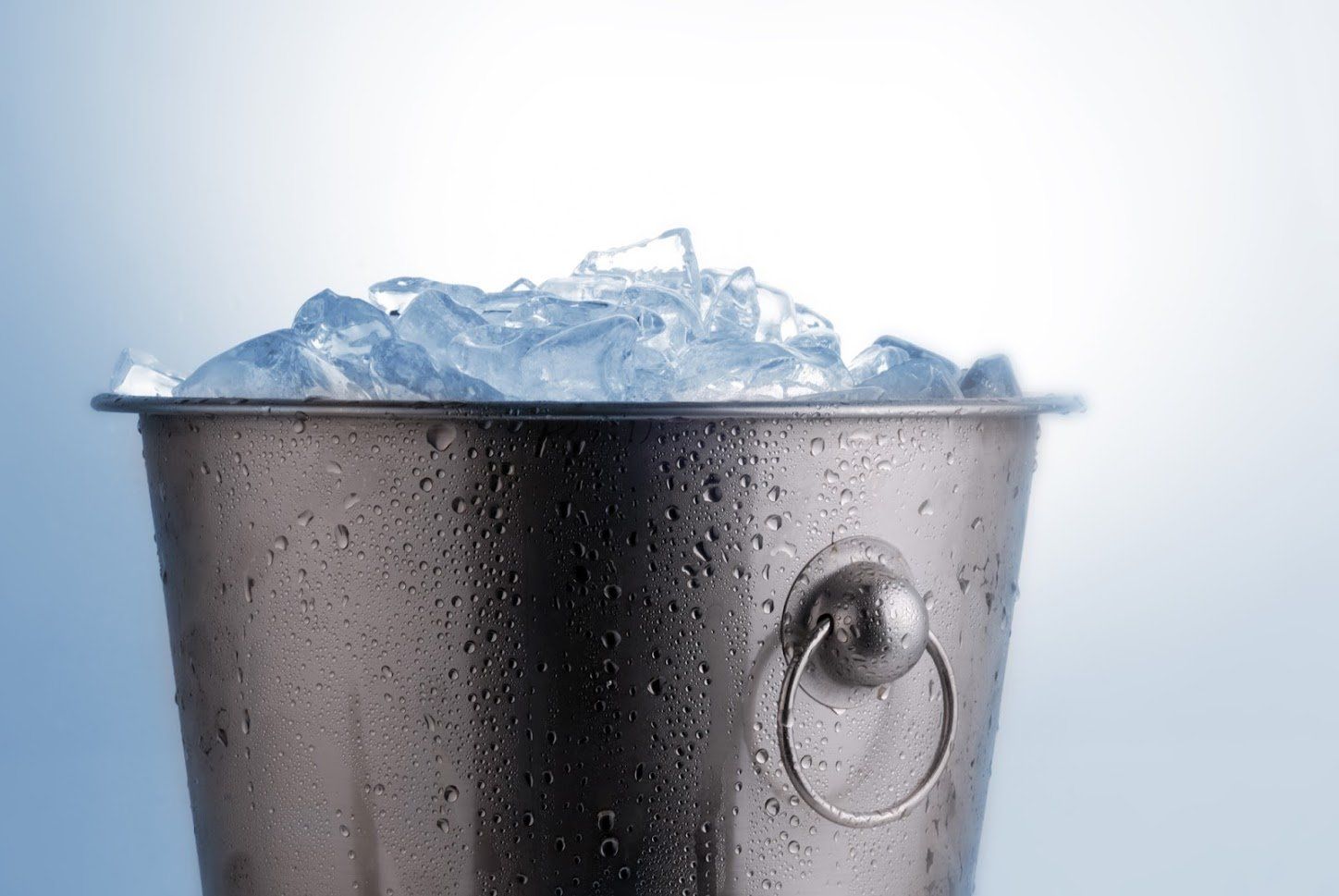 Metal ice bucket filled with ice against a blue and white background.