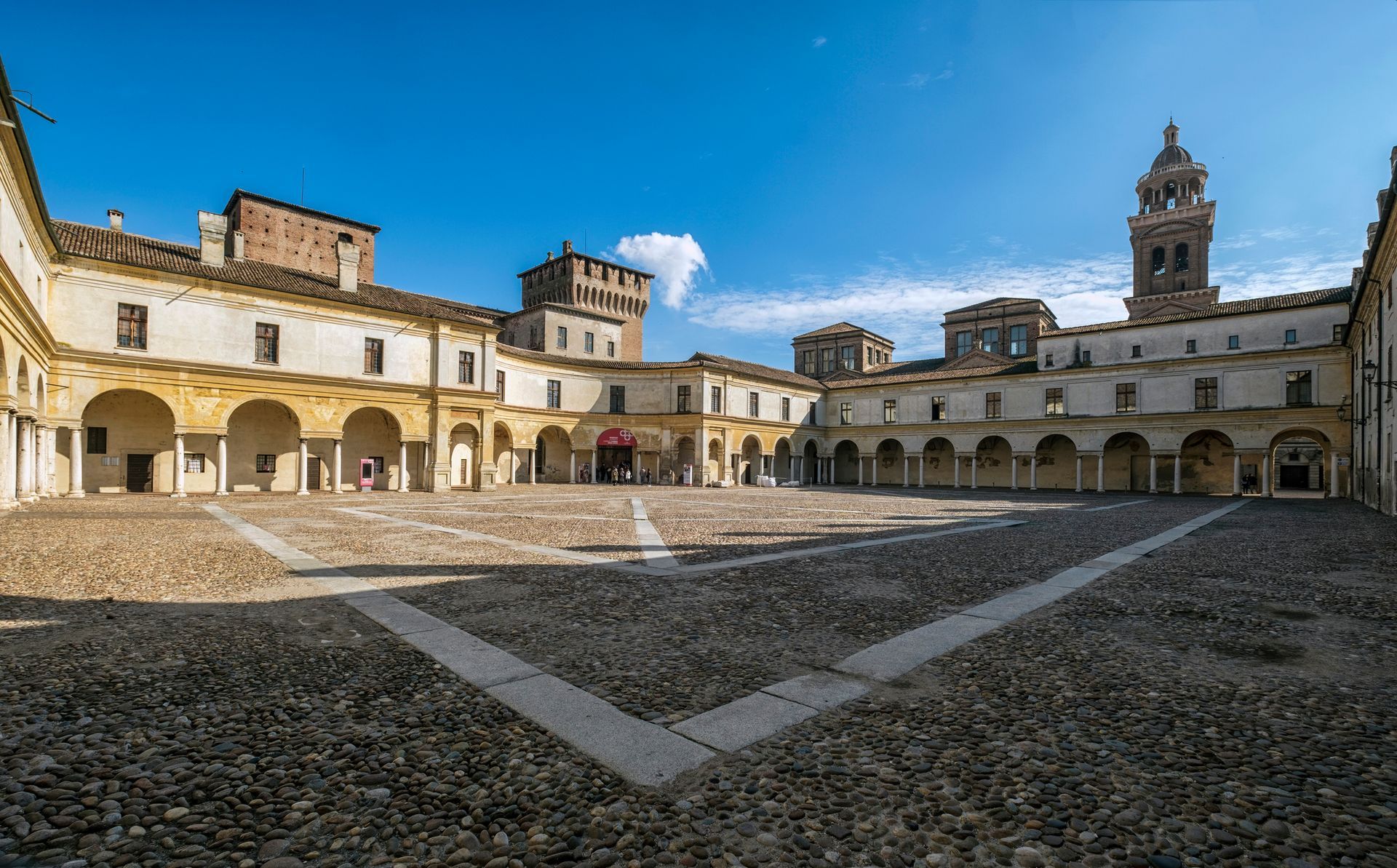 A large building with arches and a clock tower in the centre of a courtyard.