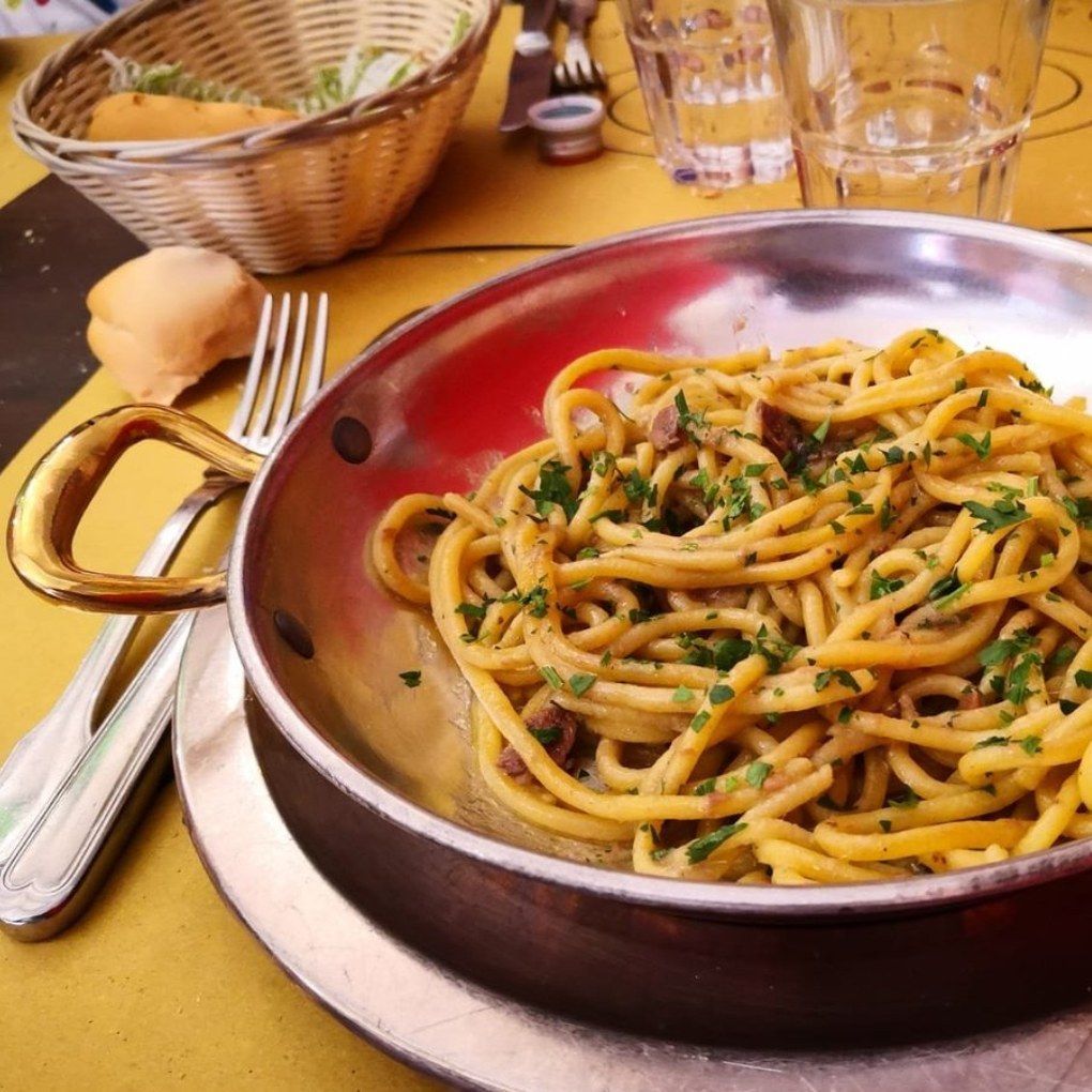 A bowl of spaghetti is placed on a table next to a basket of bread