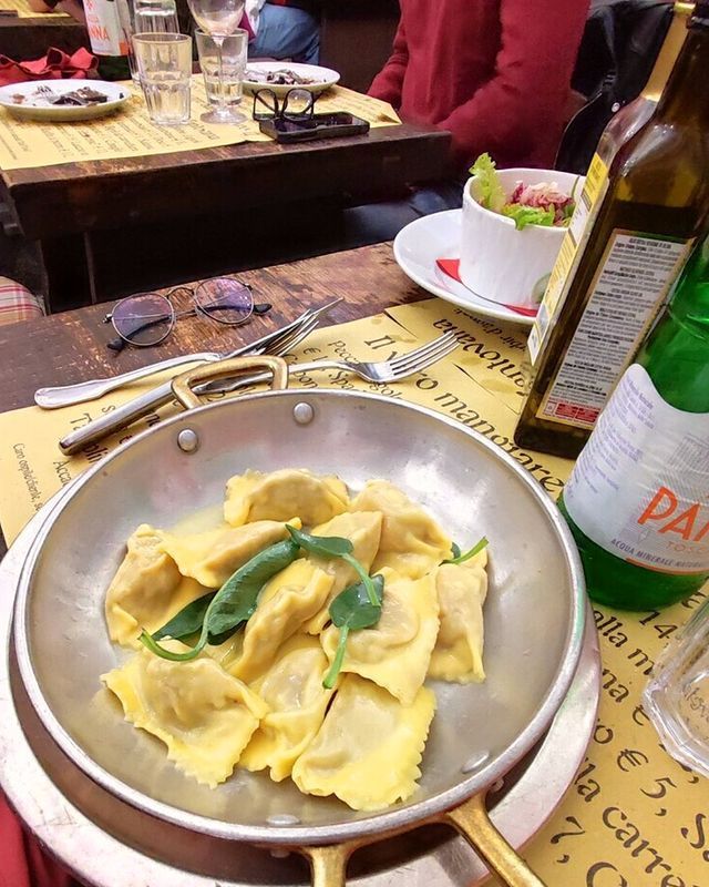 A pan of ravioli is laid on a table next to a bottle of Parma water.
