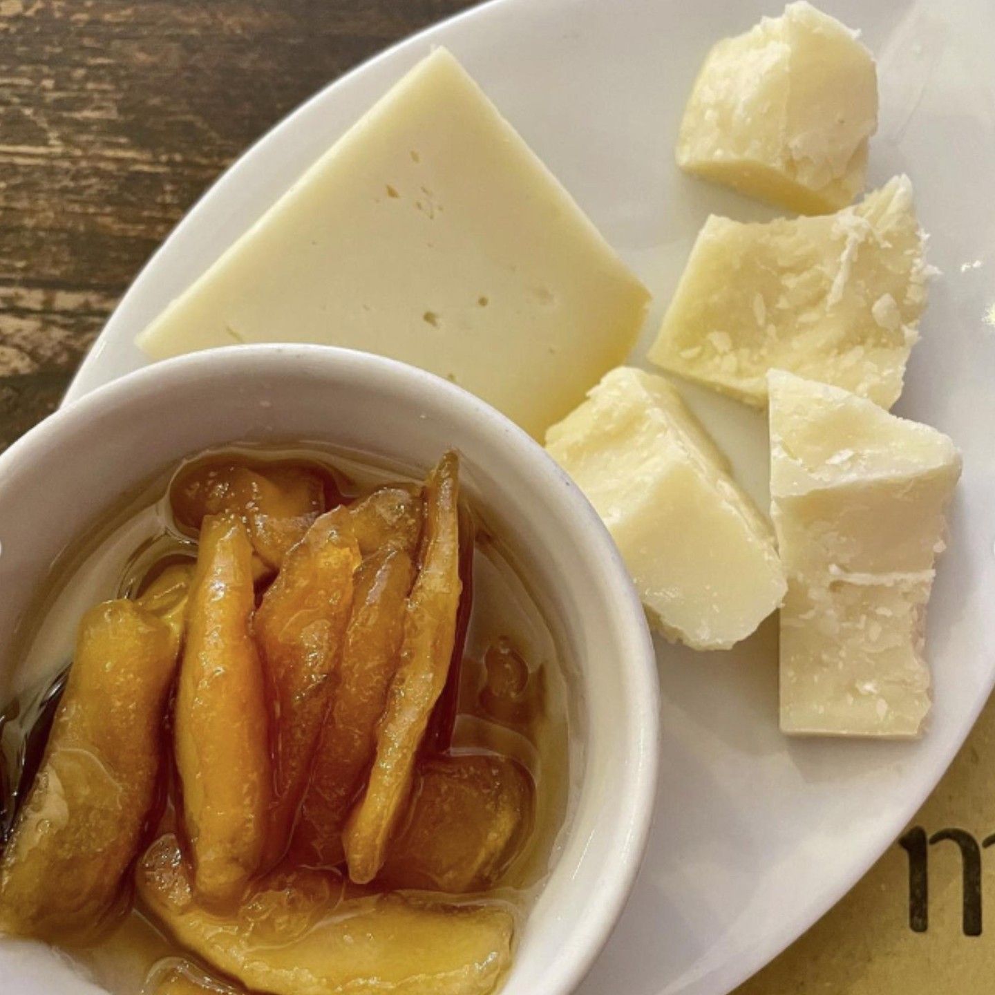 Un piatto bianco sormontato da fette di formaggio e una ciotola di sottaceti