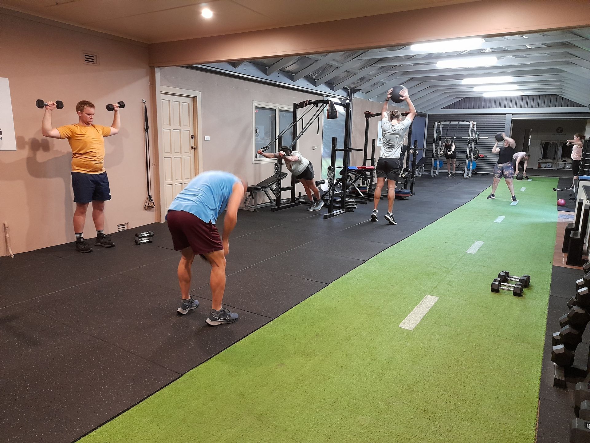 People exercising in a gym beside a green turf lane and weights.