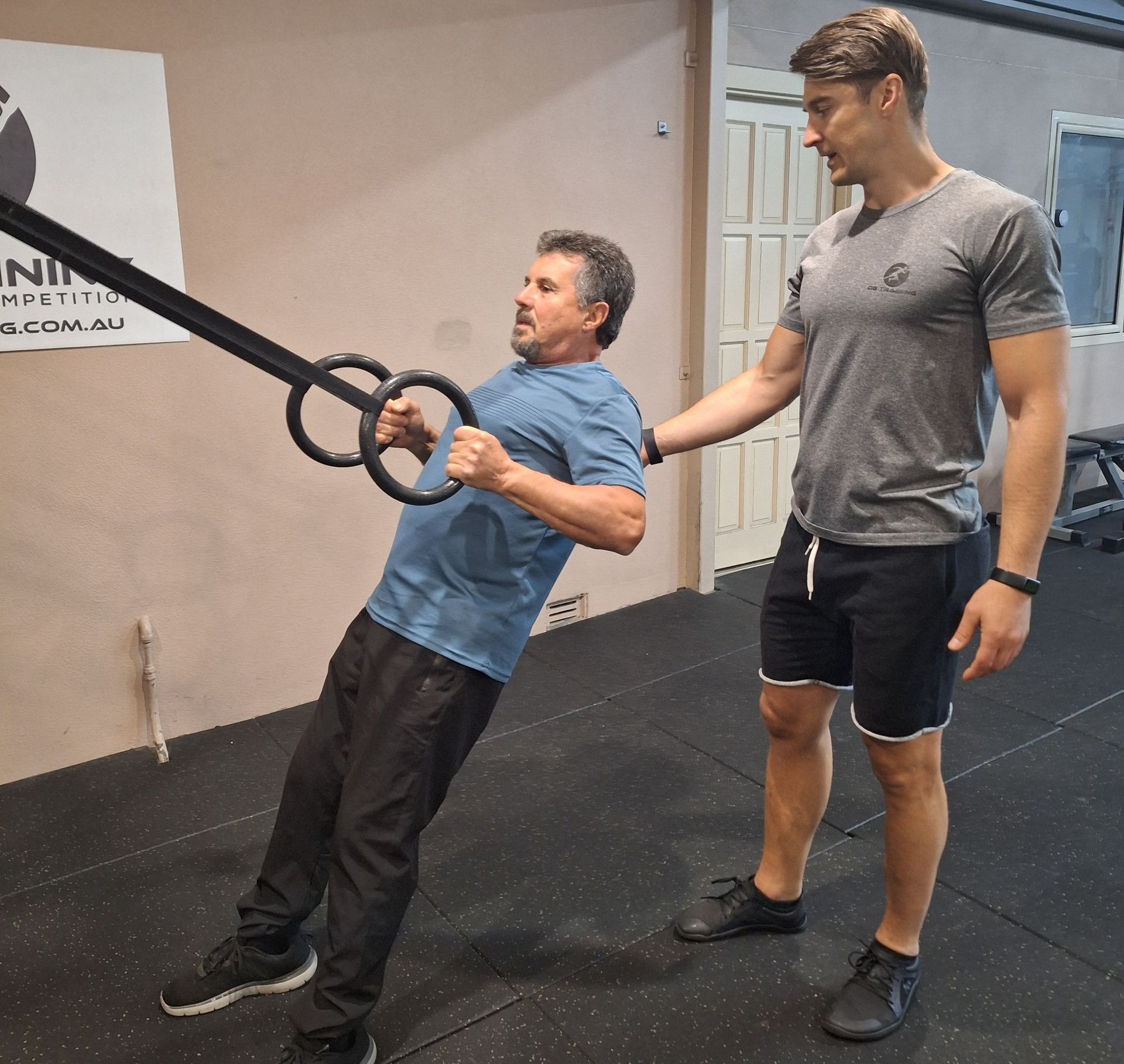 Man doing suspension rows with straps while a trainer spots him in a gym
