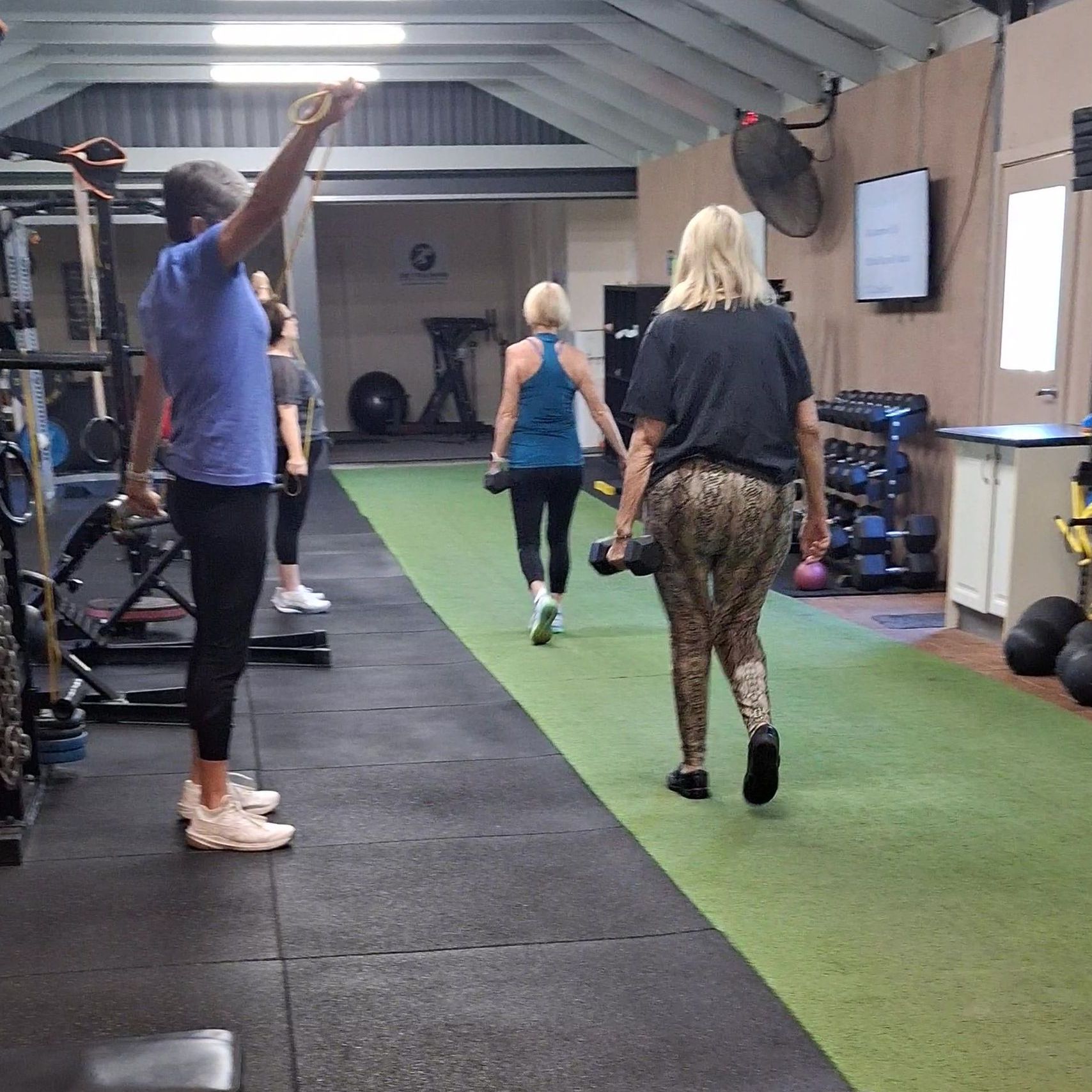 People exercising on indoor turf in a gym, with one person stretching and others walking away.