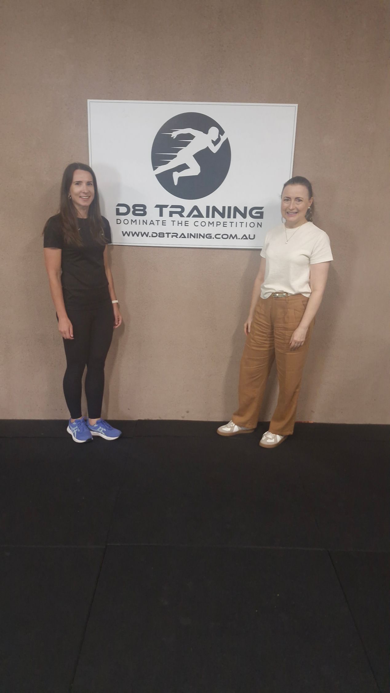 Two women are standing next to each other in front of a sign.