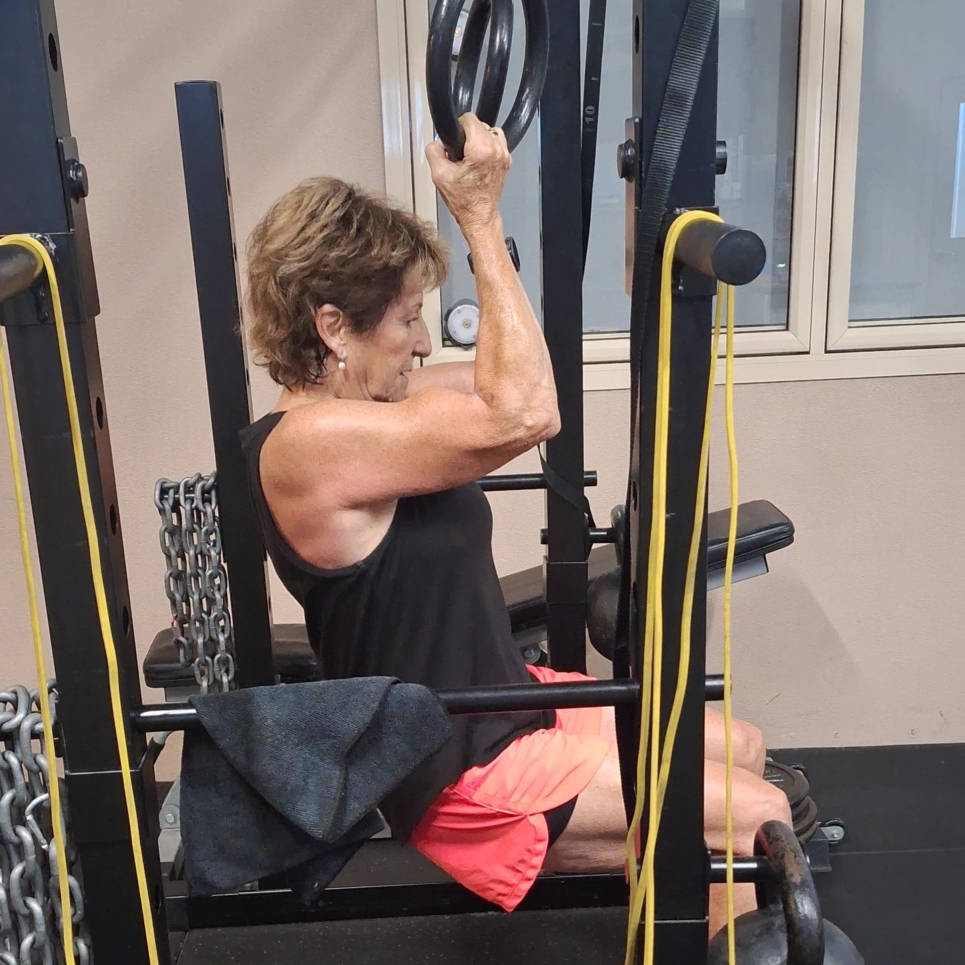 Woman doing a seated cable pulldown exercise in a gym, wearing a black tank top and pink shorts.