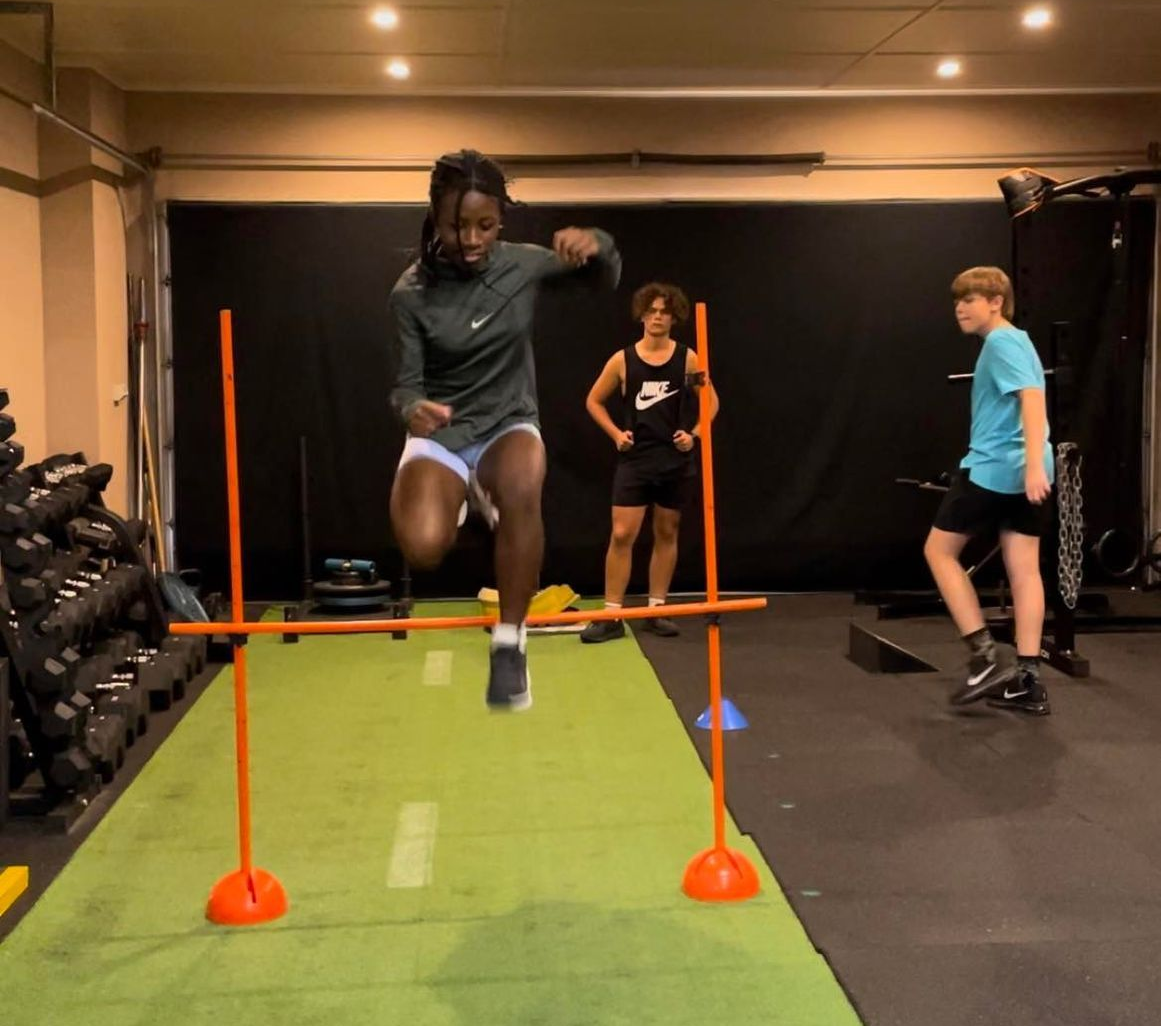 Three people doing dumbbell wall sits against a tan wall, indoors.