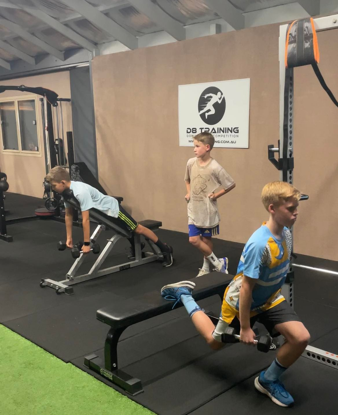 Three people doing dumbbell wall sits against a tan wall, indoors.