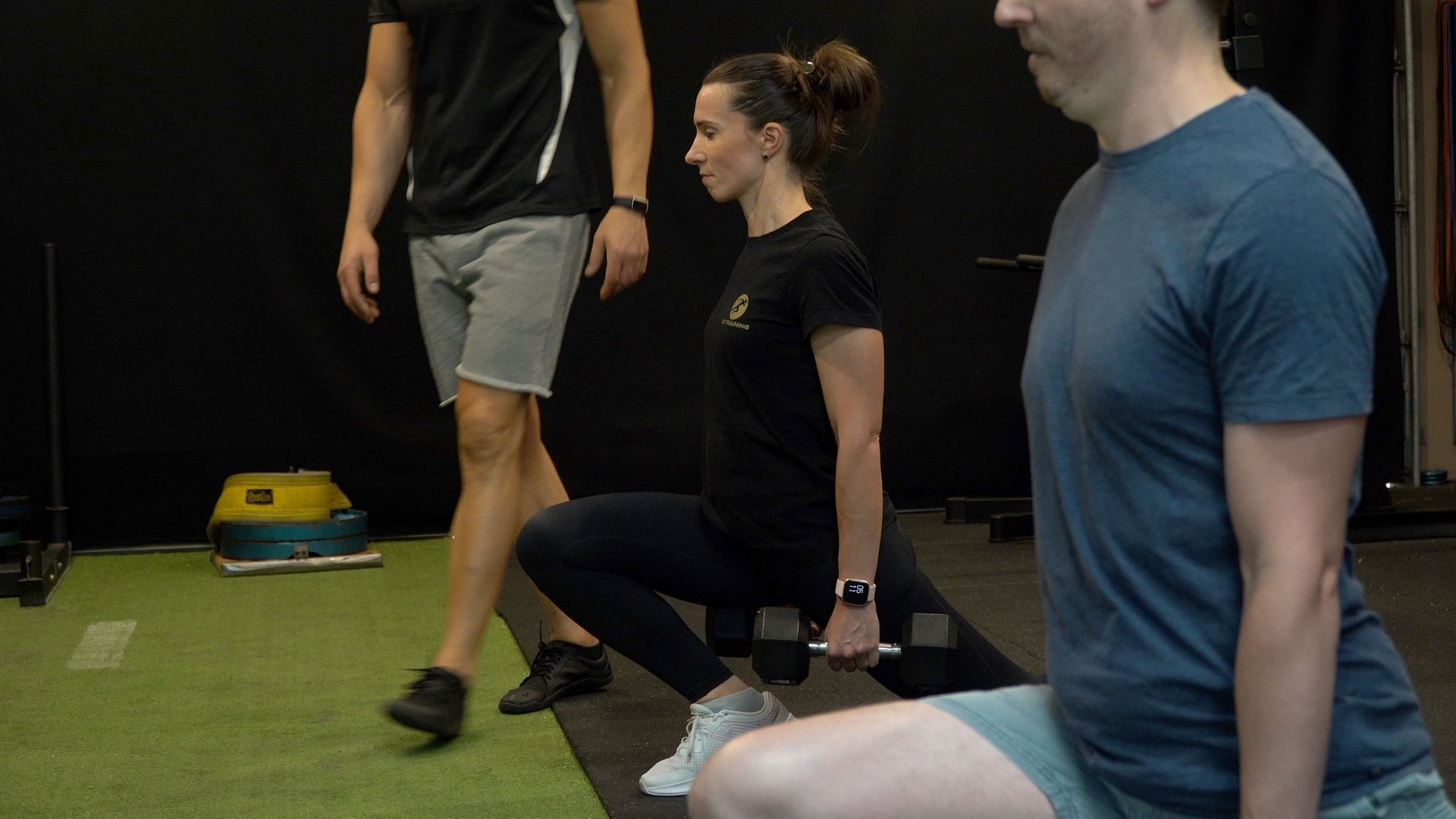 People doing lunges in a gym with turf flooring and black walls