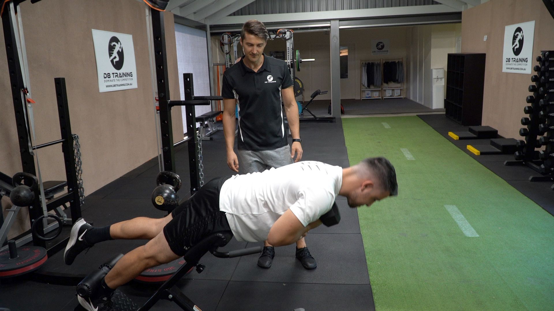 Man performing a back extension exercise with trainer supervision in a gym.