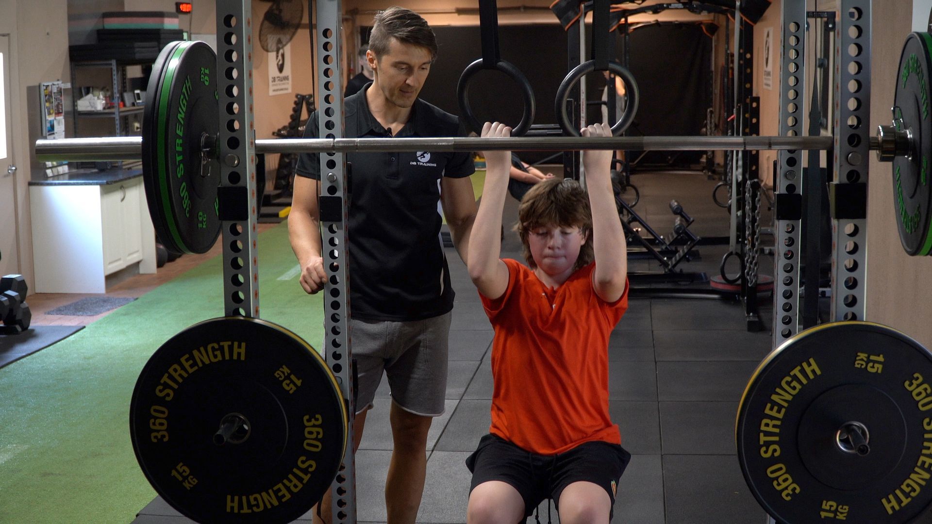 Three people doing dumbbell wall sits against a tan wall, indoors.