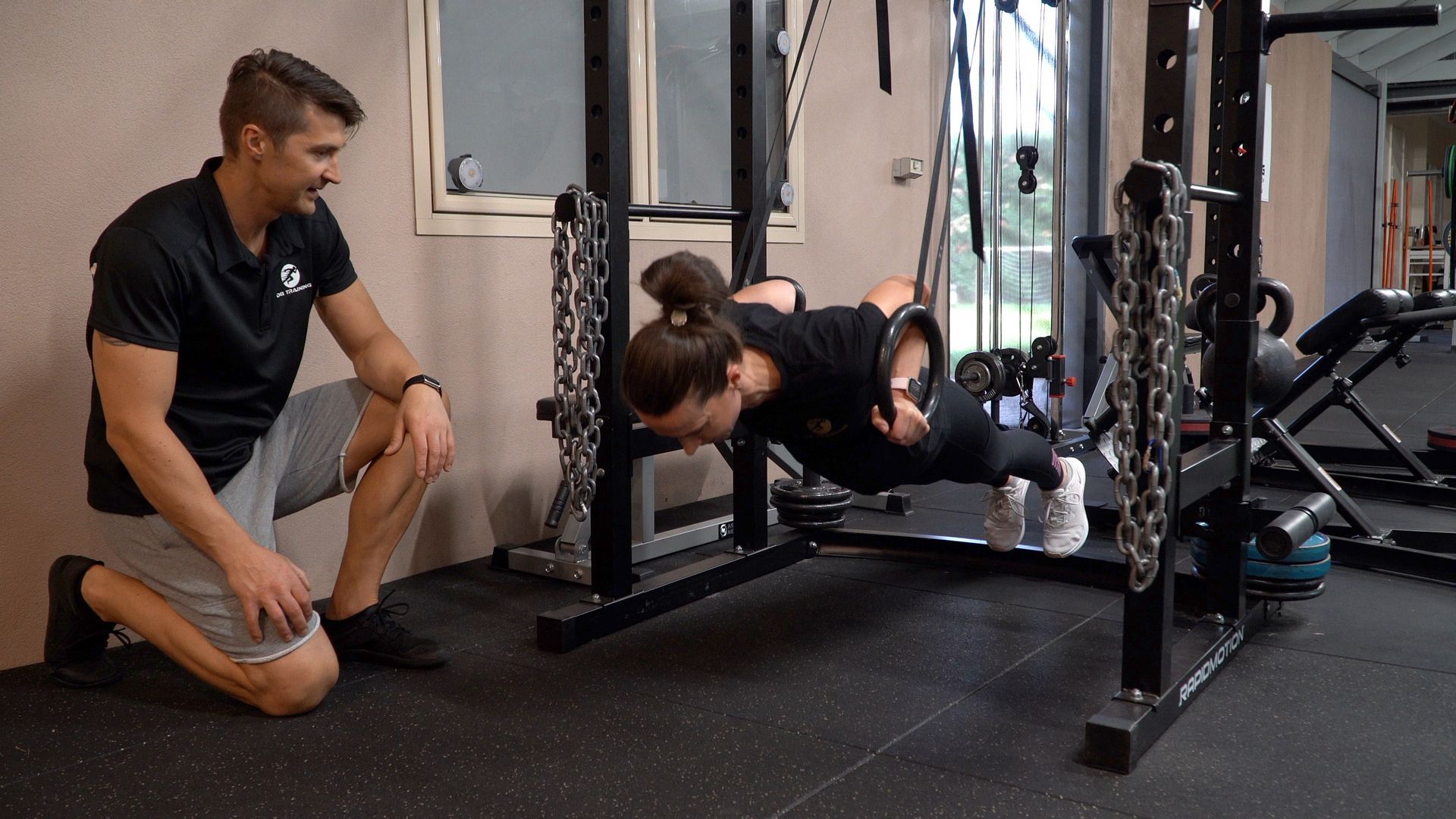 Trainer assisting woman doing push-up on gym floor near weight rack