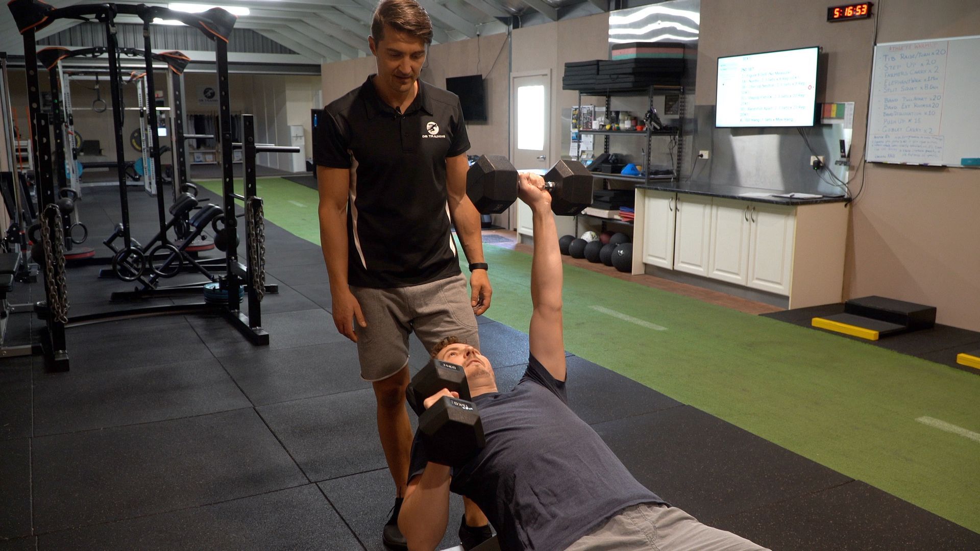 Trainer assisting a person doing a dumbbell floor press in a gym