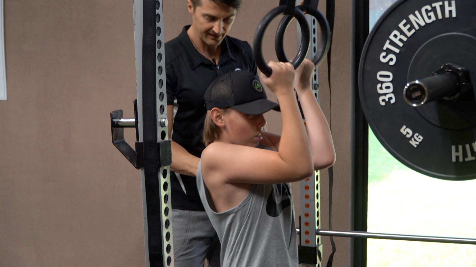 Person doing a cable workout in a gym, with a trainer behind and weight plates visible.