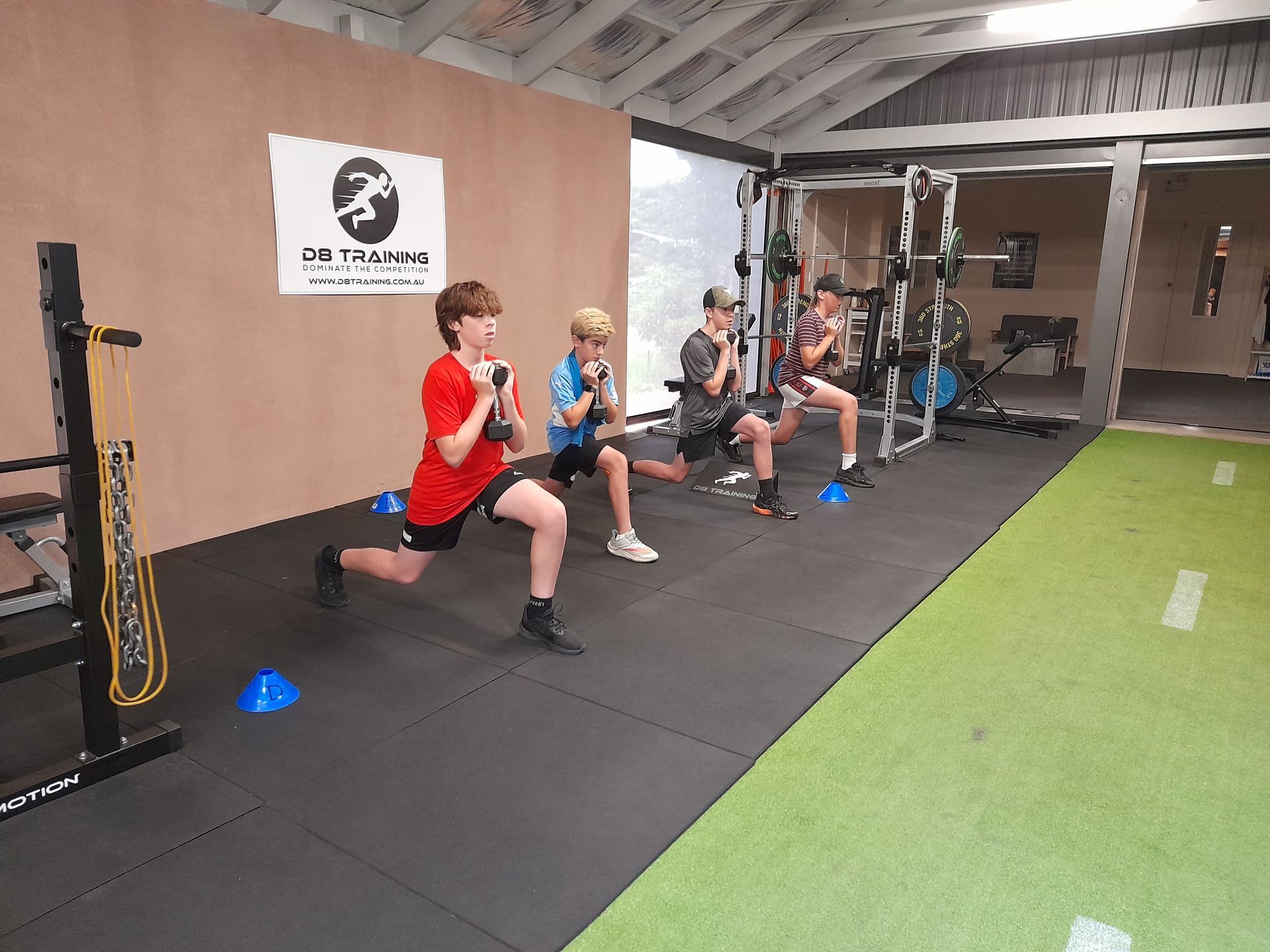 Three people doing dumbbell wall sits against a tan wall, indoors.