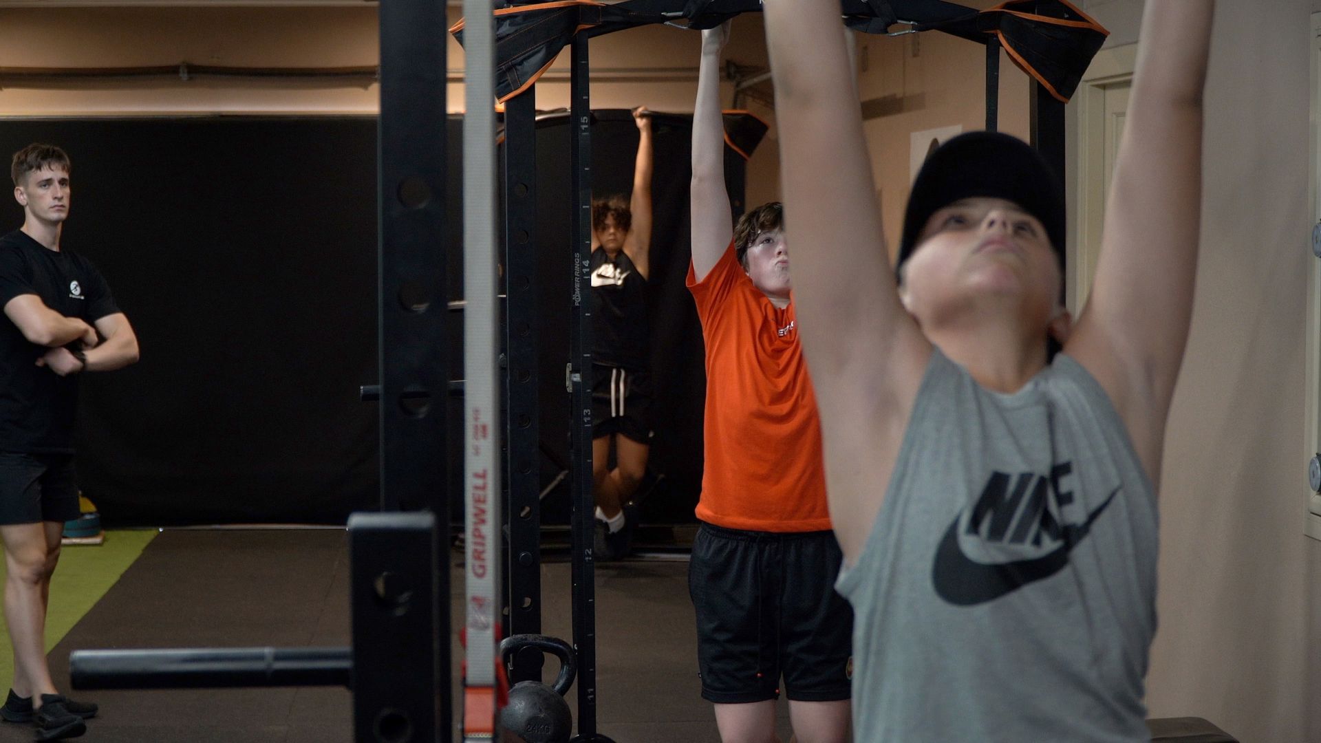 People exercising in a gym, hanging from pull-up bars and stretching near a cable machine.