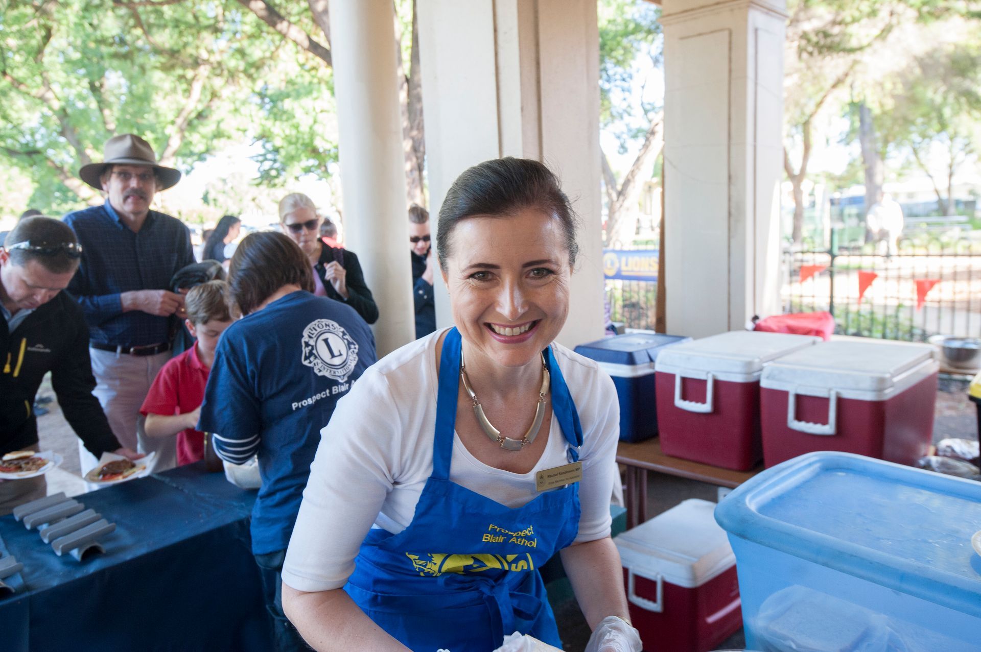 A woman in a blue apron is standing in front of a table.
