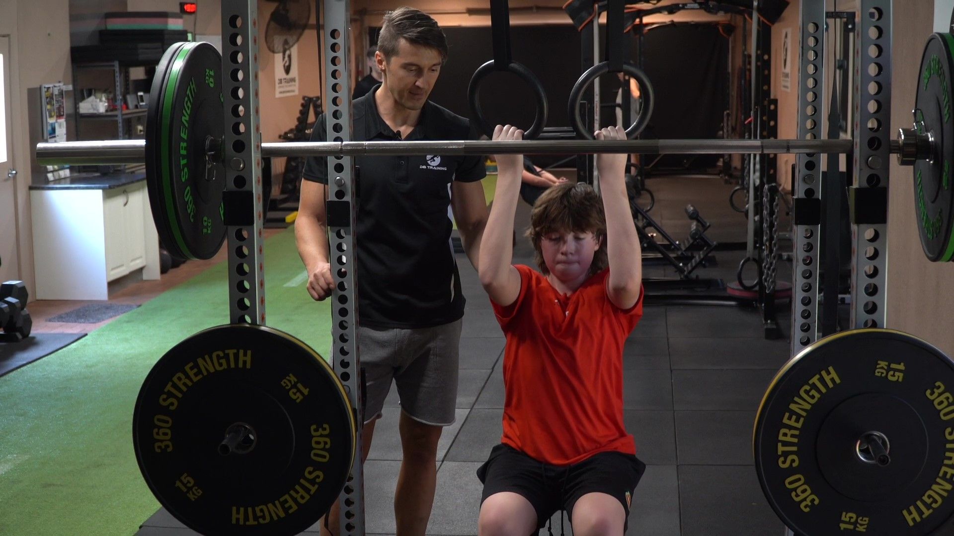 Weightlifter doing a seated overhead press while a spotter stands behind in a gym.